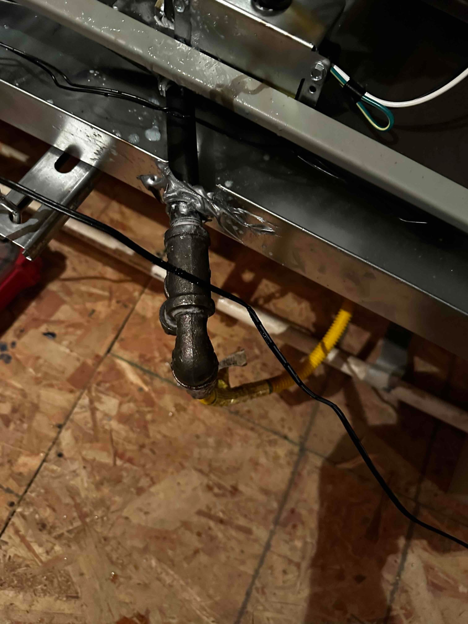 Gas piping with sediment trap and flexible connector installed beneath the equipment cabinet, with sealant applied at the penetration.
