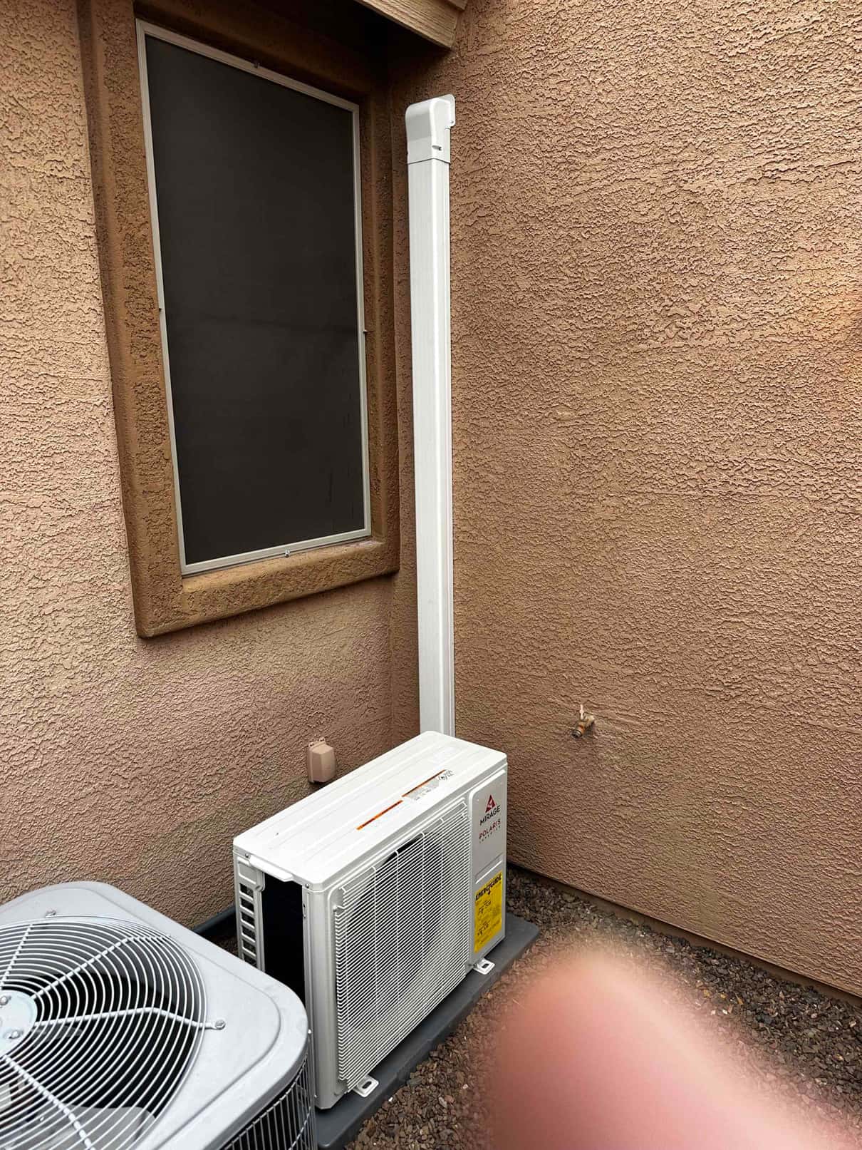 Mini-split outdoor condenser set on a level pad with line set neatly routed in a wall-mounted cover.