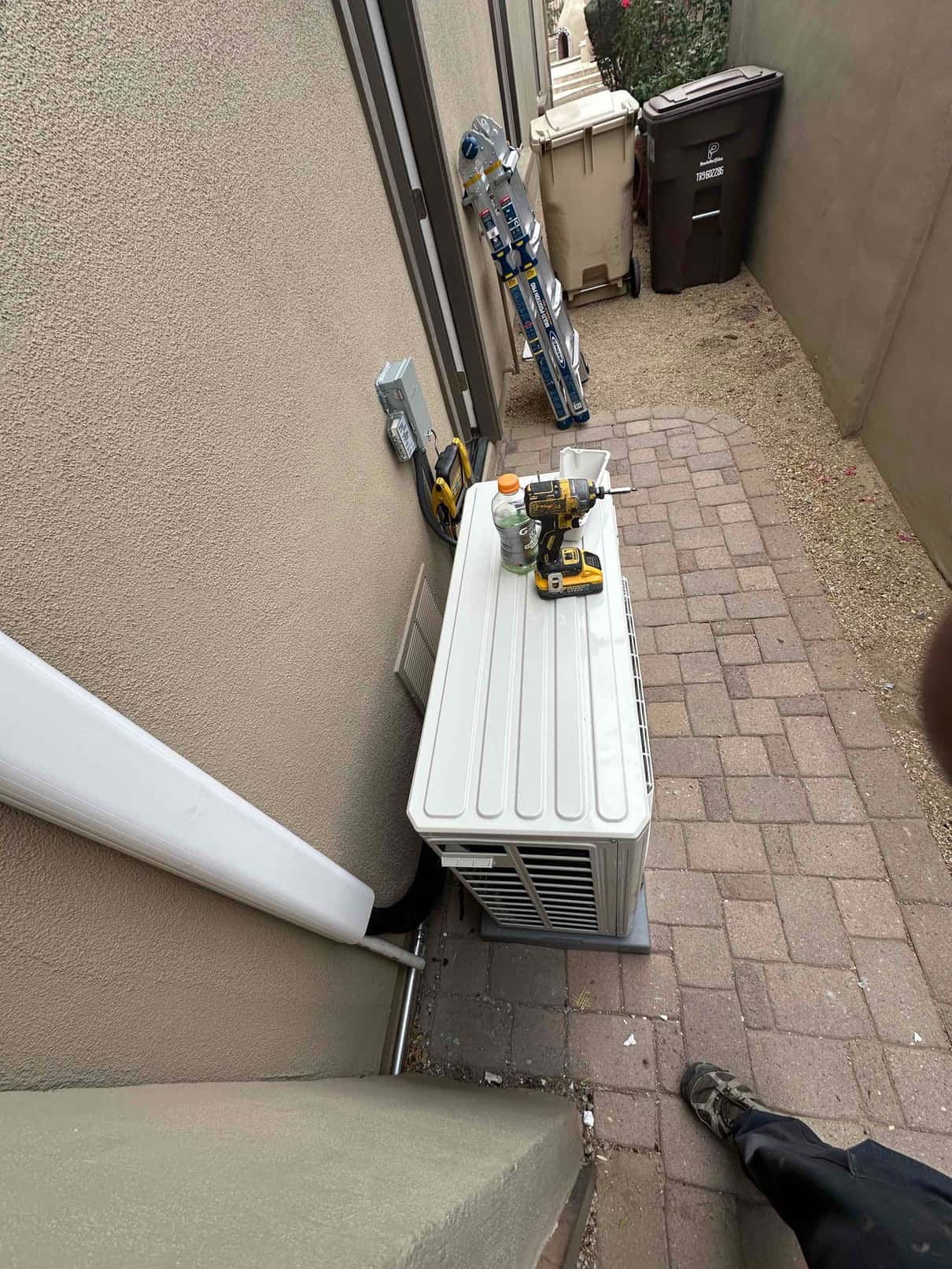 Mini-split outdoor unit set on a pad with line-hide conduit and disconnect installed along the exterior wall.