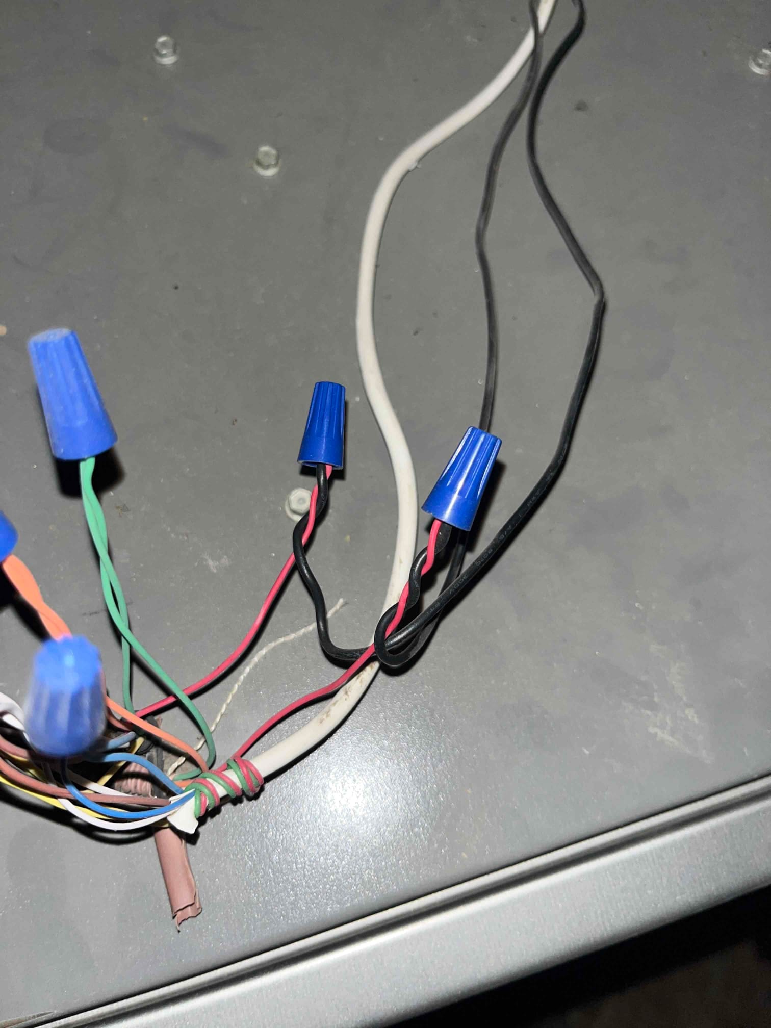 Multiple low-voltage and line-voltage wires joined with blue wire nuts inside an HVAC unit junction area.