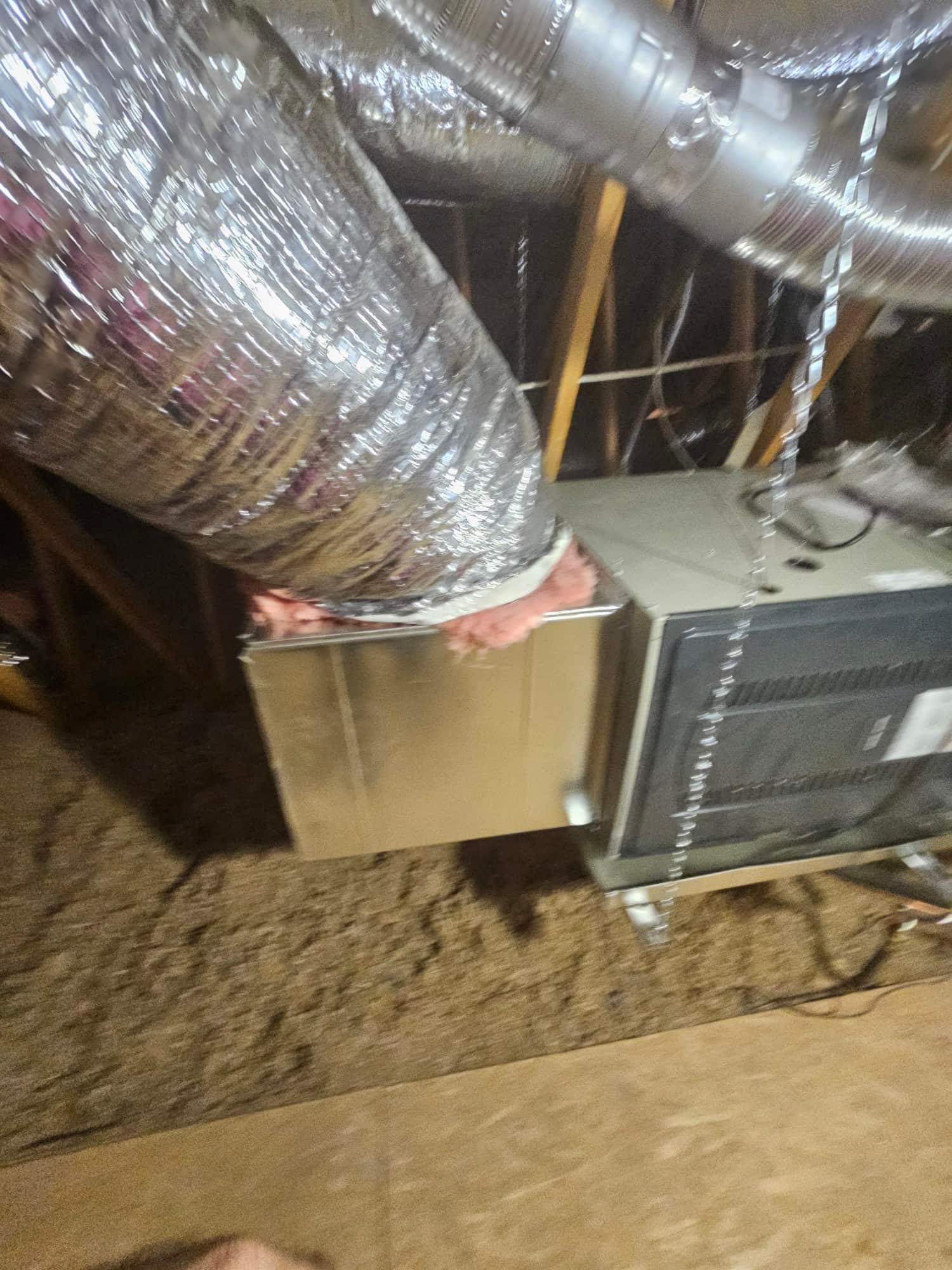 New air handler connected to insulated flex duct and metal duct transitions in the attic, with suspension straps supporting the unit.