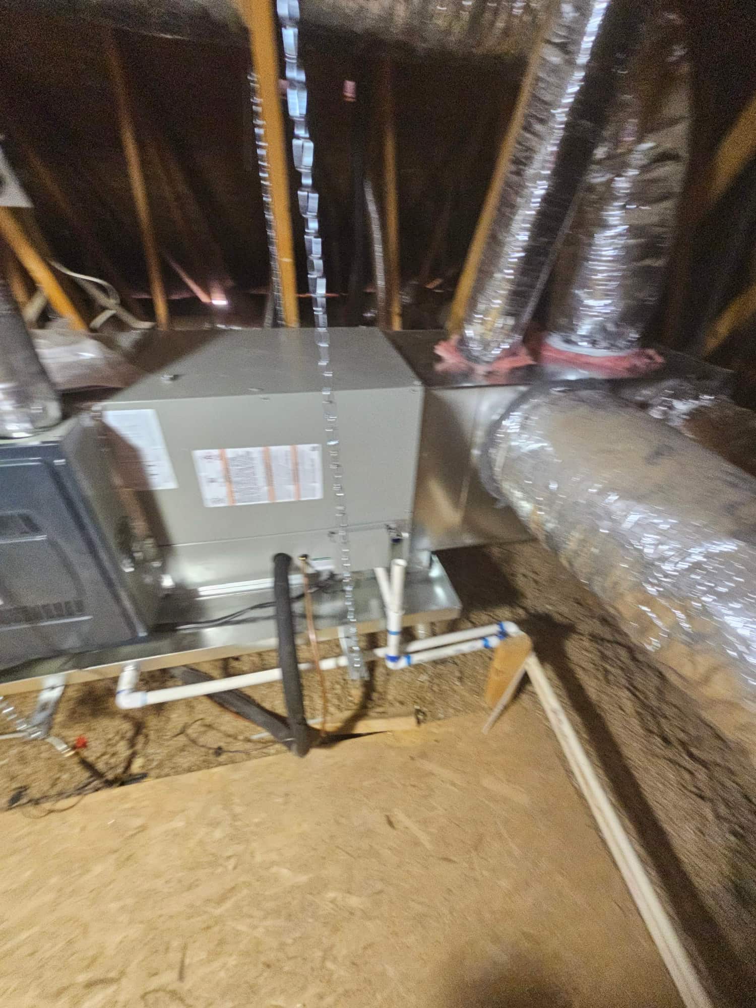 New air handler set in attic with connected ductwork, insulated refrigerant line, and PVC condensate drain with trap installed.