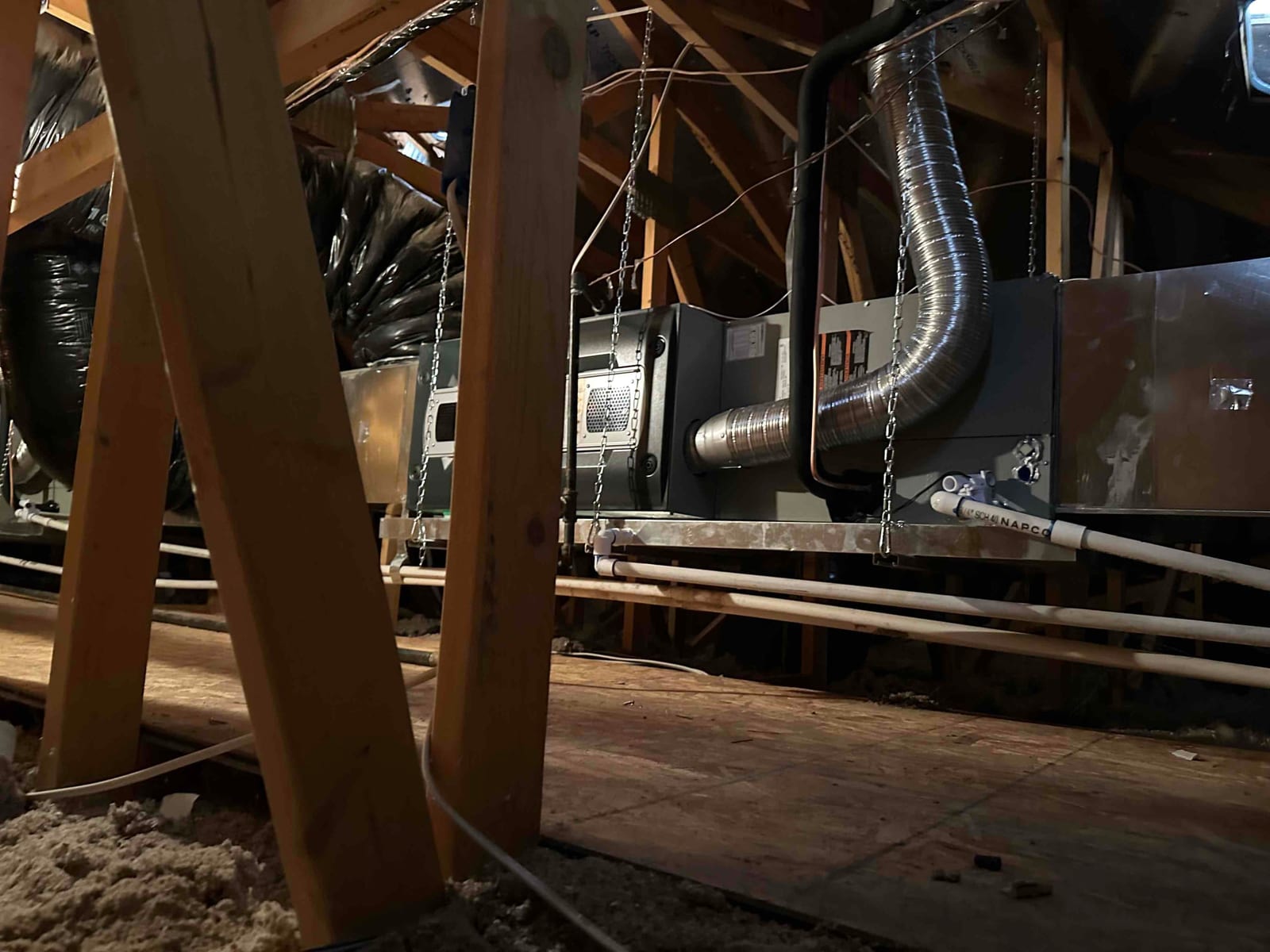 New attic air handler installation suspended with chains, connected to ductwork, insulated refrigerant line, and condensate drain piping.