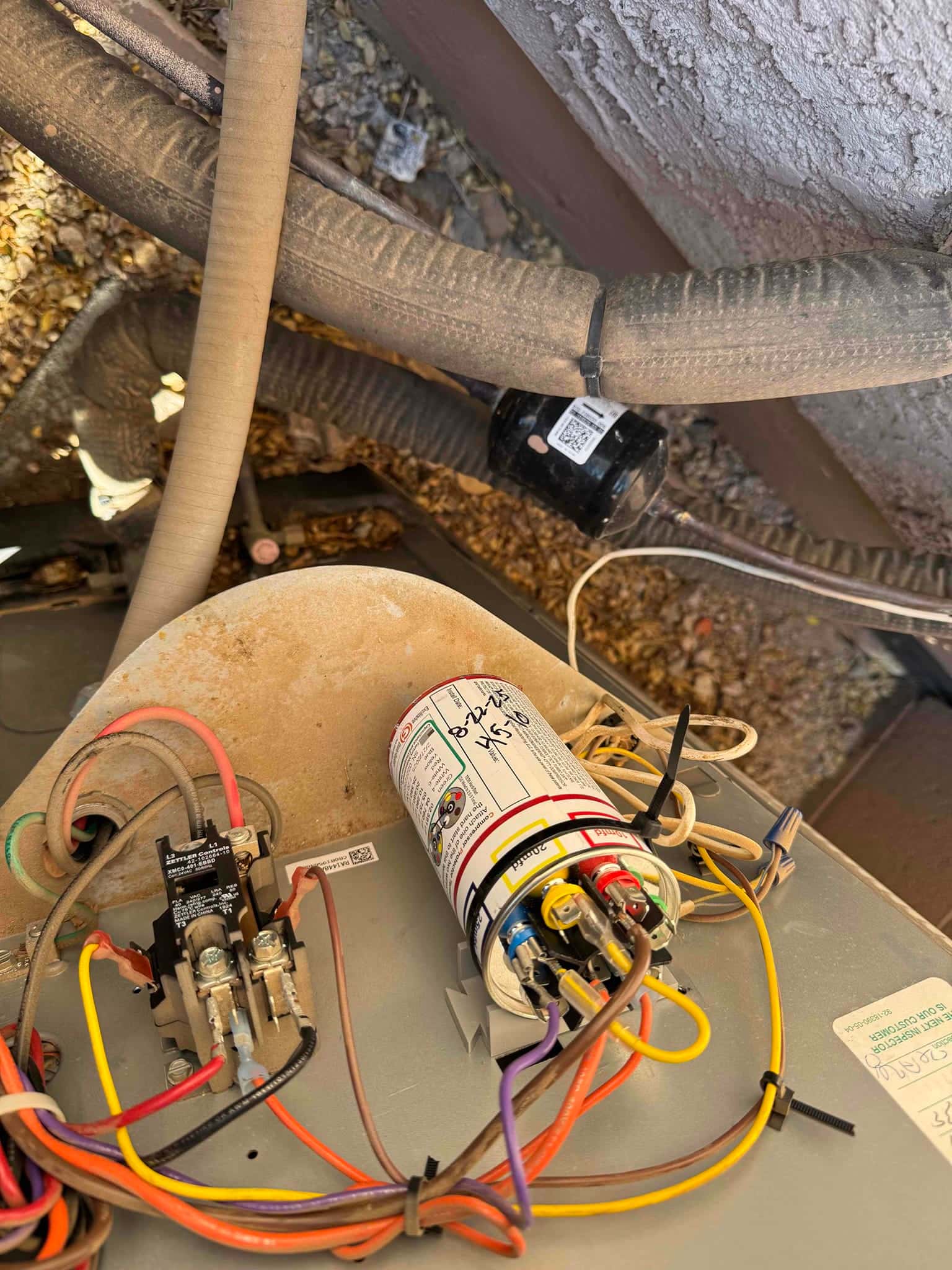 New dual-run capacitor installed with labeled terminals and reconnected wires next to the contactor inside the condenser unit.