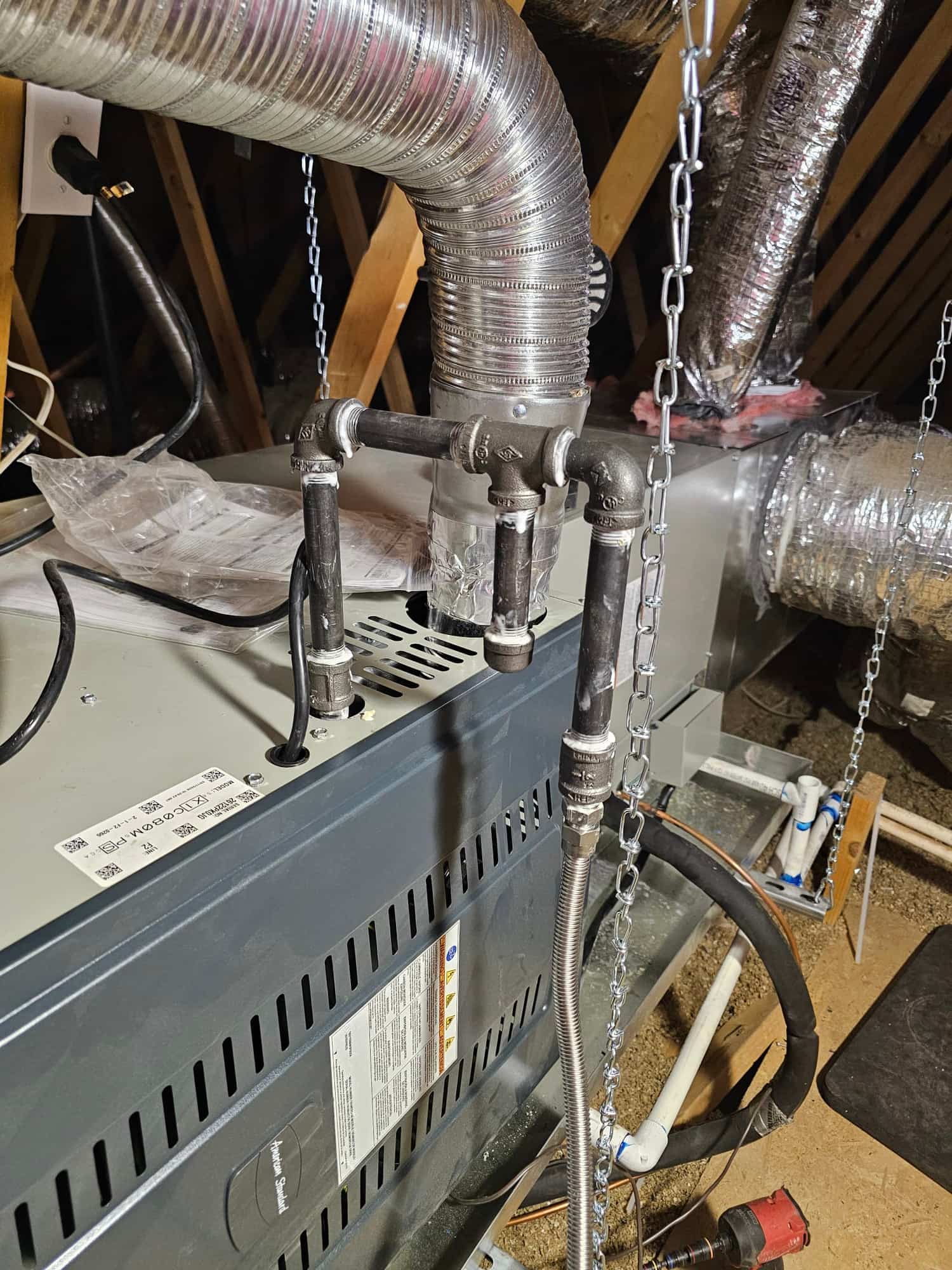 New furnace and duct connections installed in attic, with rigid vent, gas piping drip leg, condensate drain, and suspension chains.