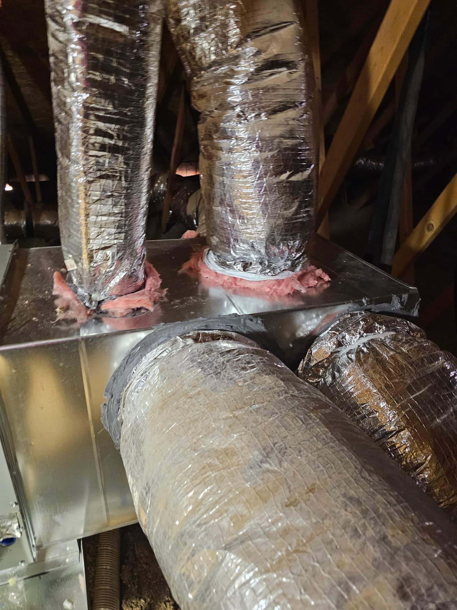 New insulated flex ducts connected and sealed to a metal plenum in the attic during HVAC installation.