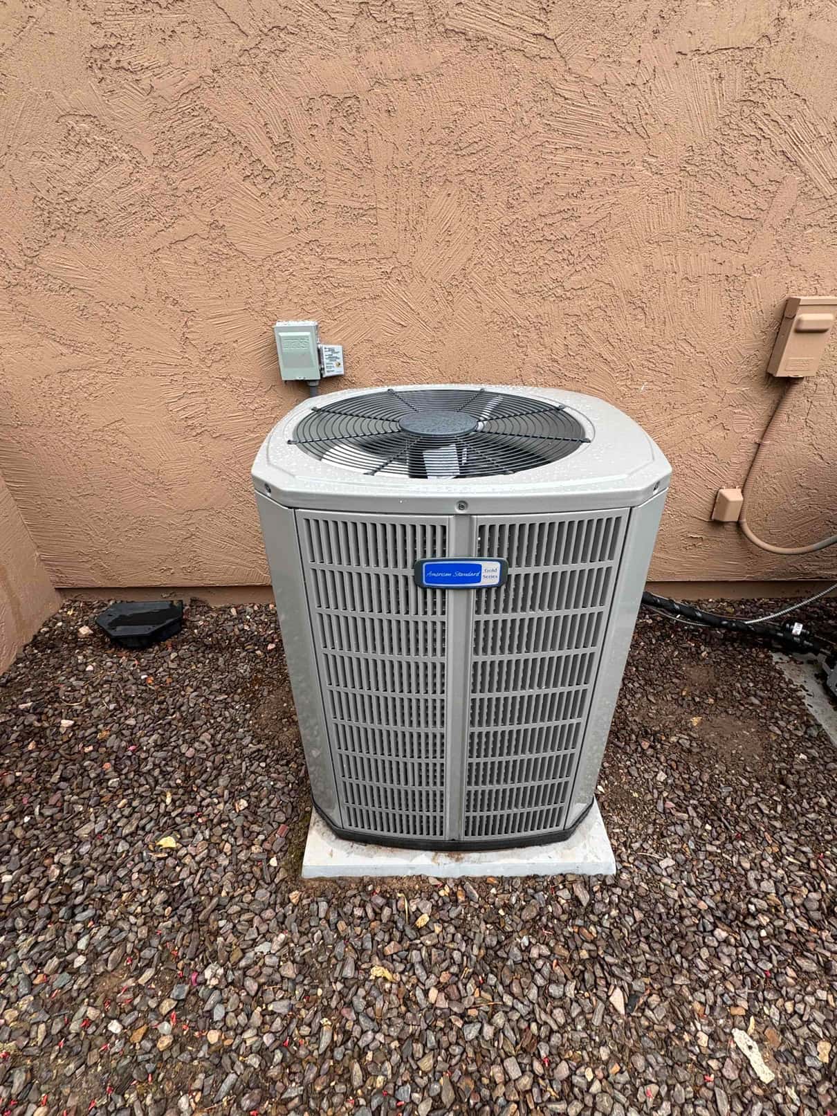 New outdoor condenser set on a level pad beside the house with electrical disconnect mounted on the wall.