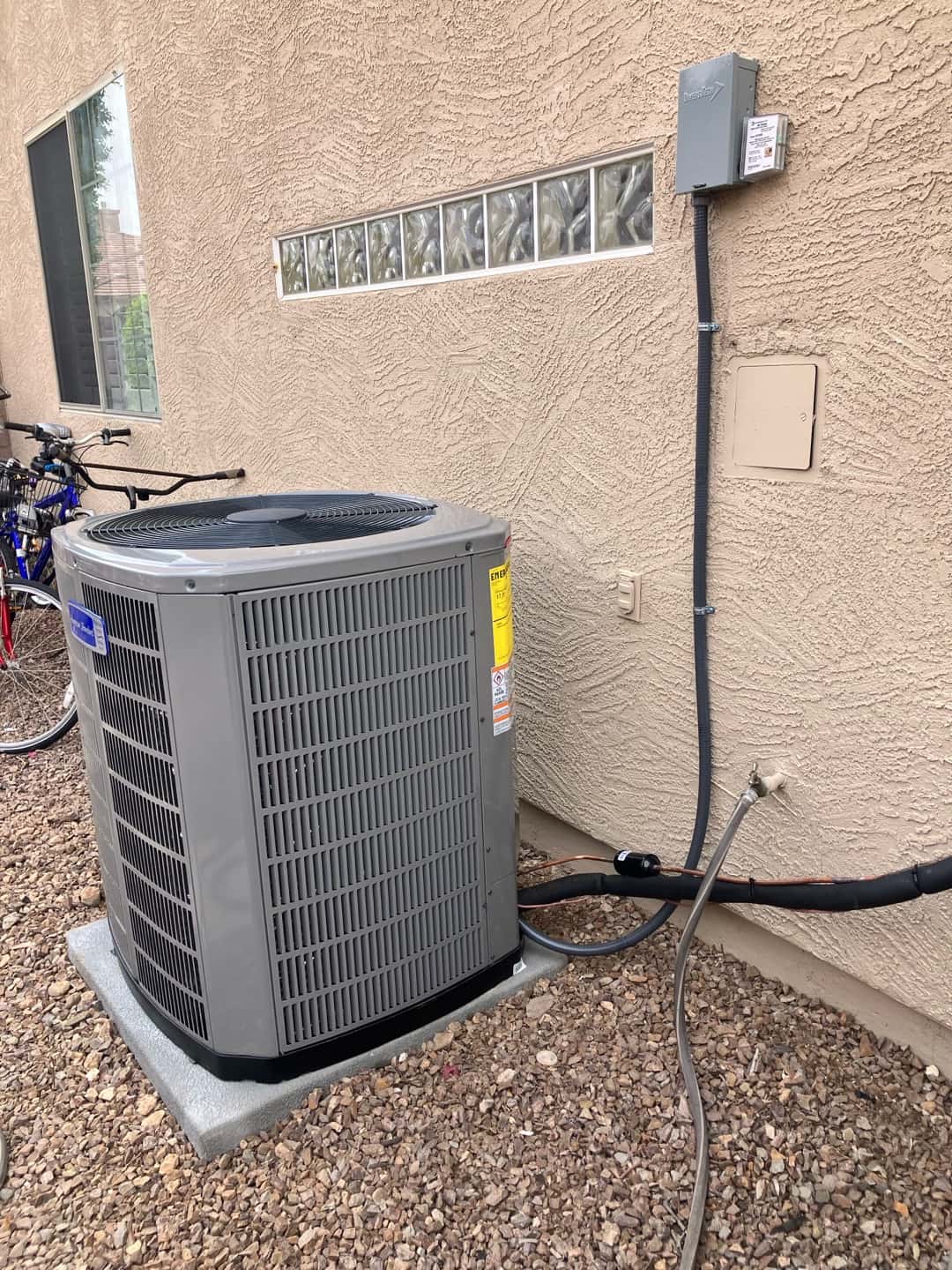 New outdoor condenser set on a level pad with insulated line set and weatherproof electrical disconnect mounted on the wall.