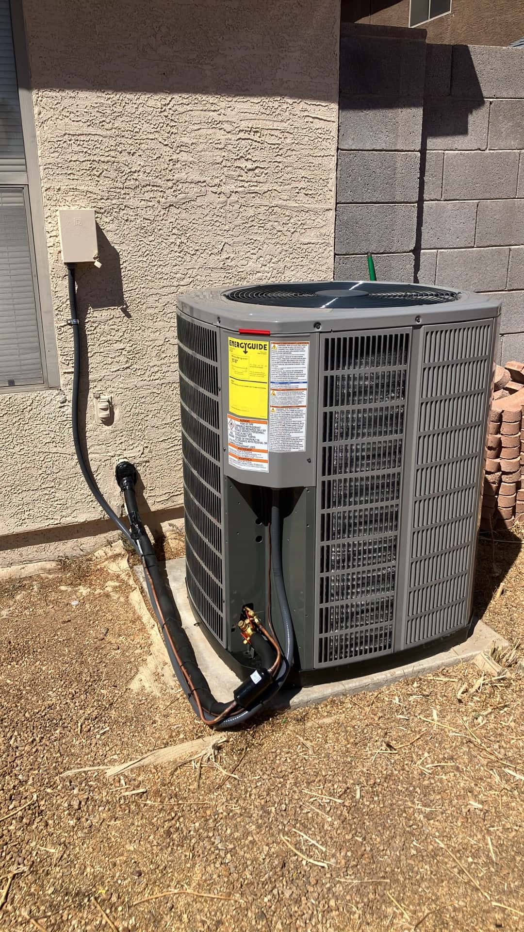 New outdoor condenser set on a level pad with insulated refrigerant lines, disconnect box, and sealed wall penetration visible.