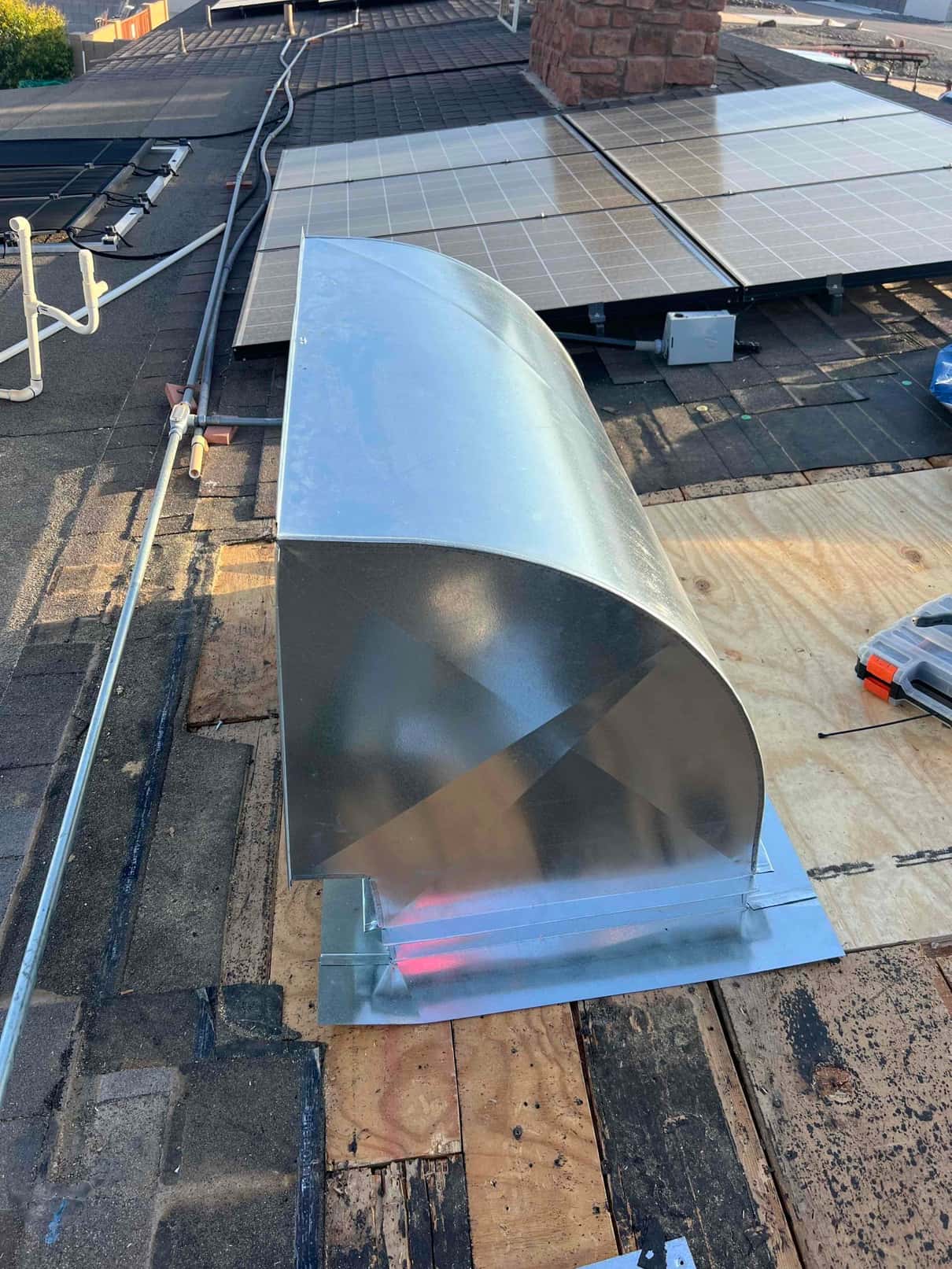 New rooftop sheet-metal hood installed on prepared decking near existing utility penetrations and solar panels, ready for final weather sealing.