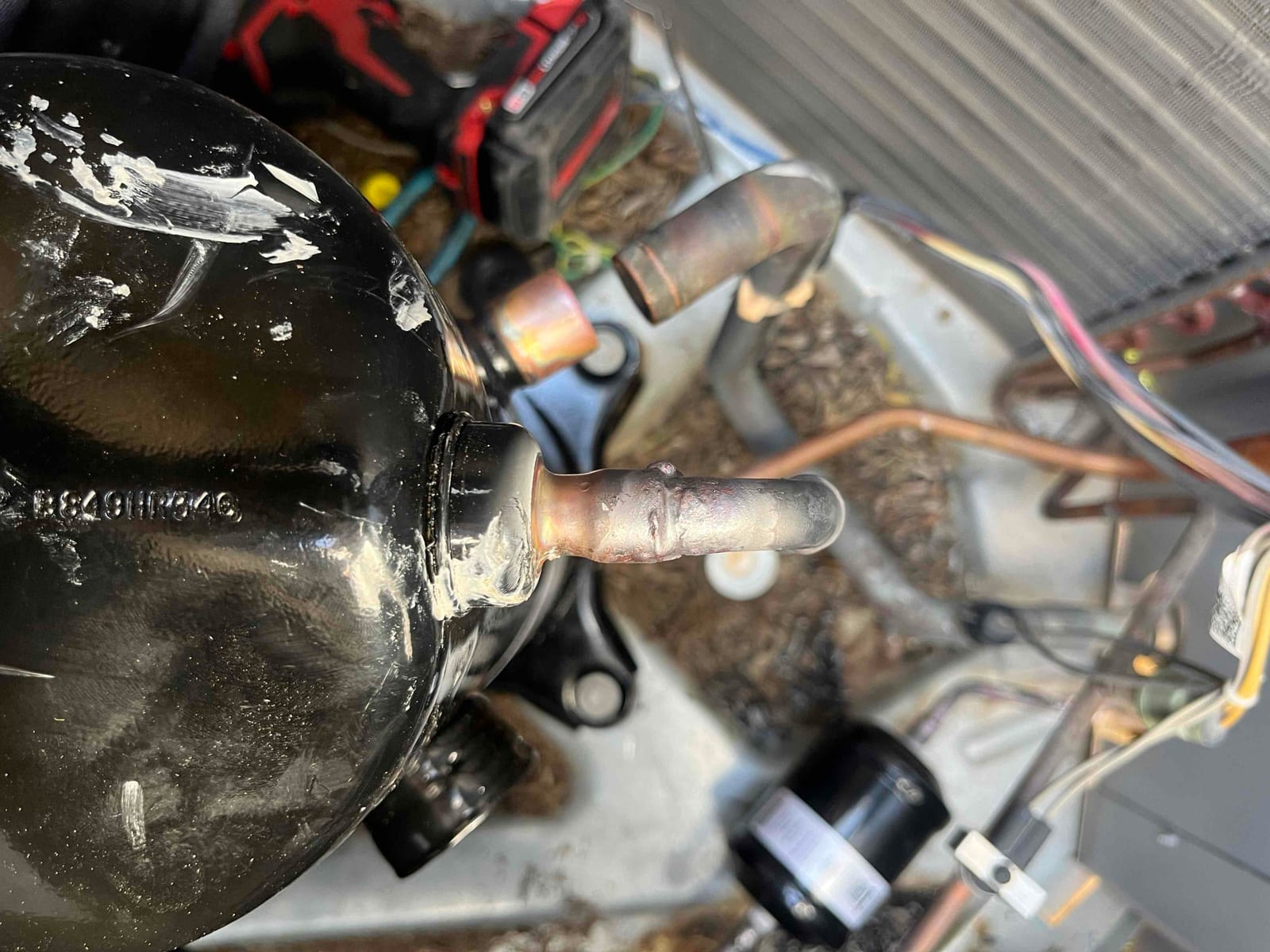 Newly brazed compressor discharge and suction stubs inside an outdoor condenser, with clean joints and surrounding wiring visible.