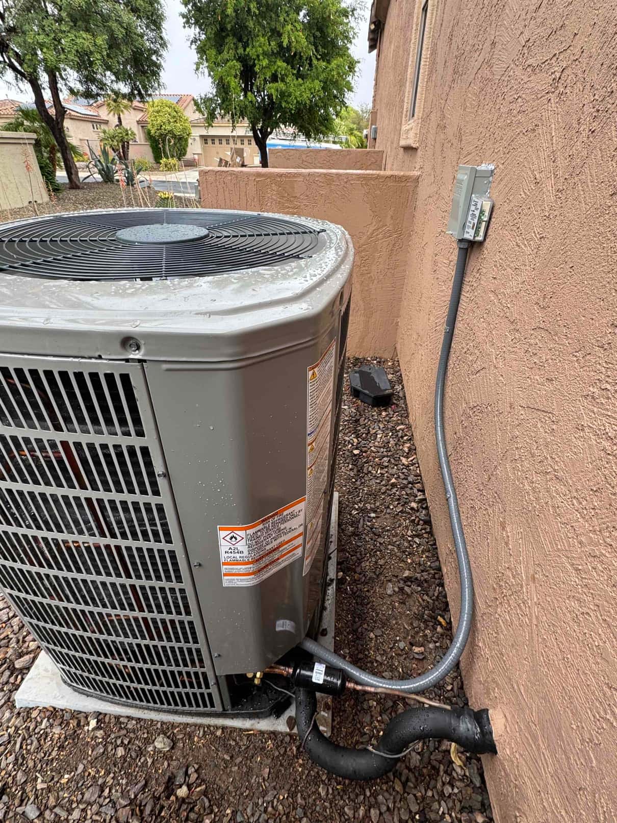 Outdoor condenser set on a level pad with insulated refrigerant line set and weatherproof electrical disconnect mounted on the wall.