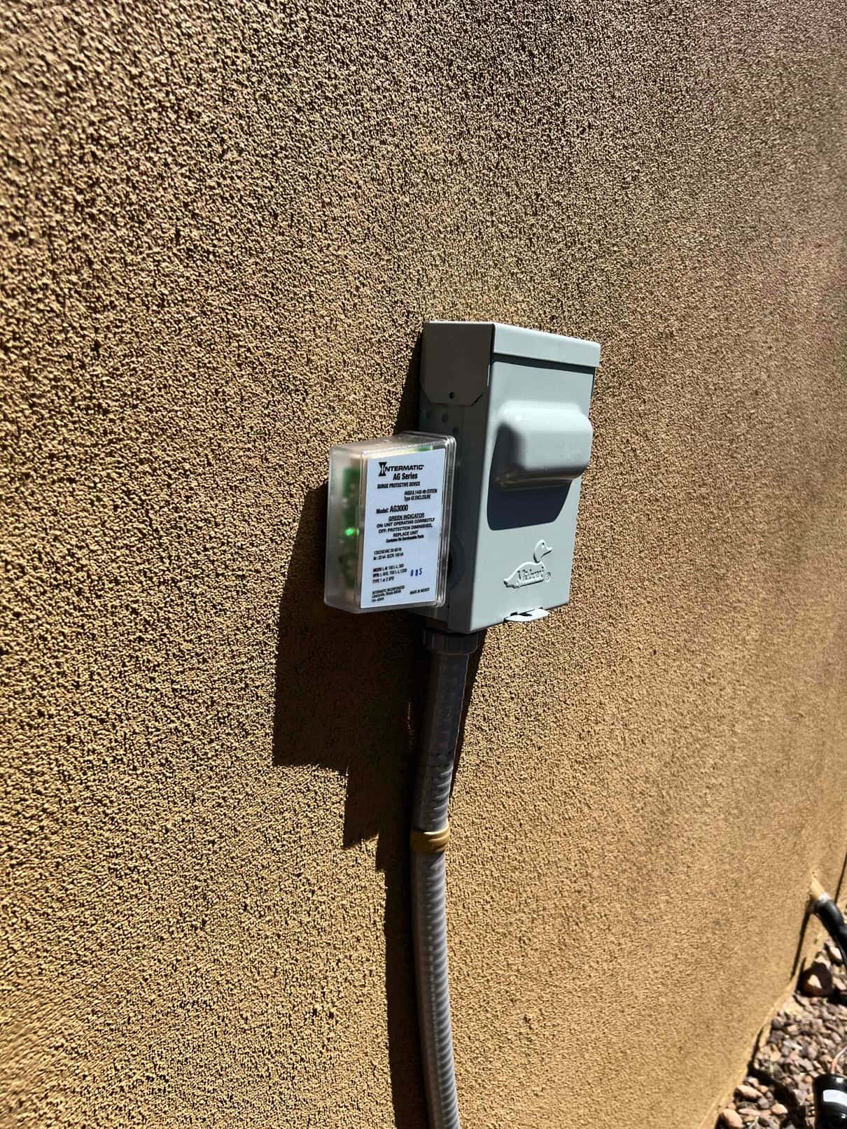 Outdoor HVAC disconnect with surge protection mounted on stucco wall, flexible metallic conduit routed to the condenser location.