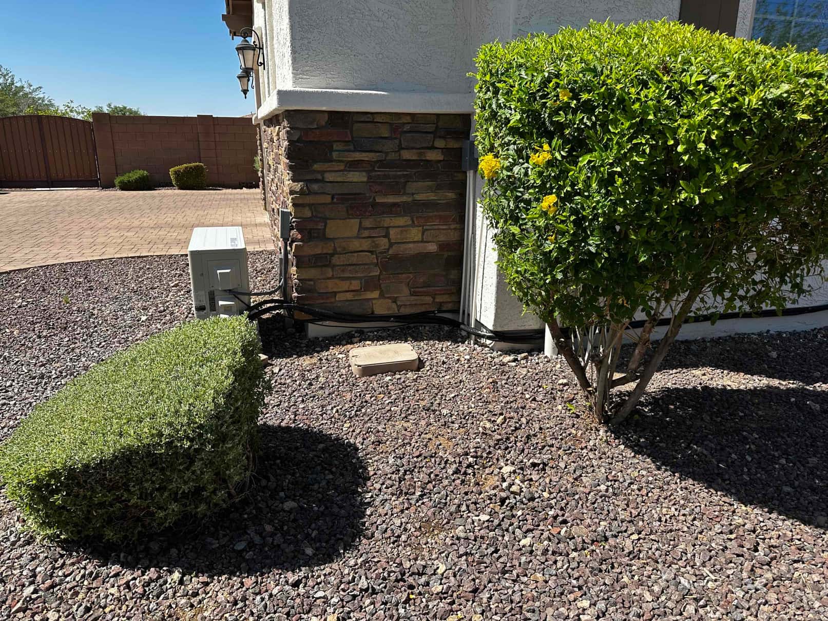 Outdoor mini-split condenser set on a patio area with insulated line set and sealed wall penetration along the house exterior.