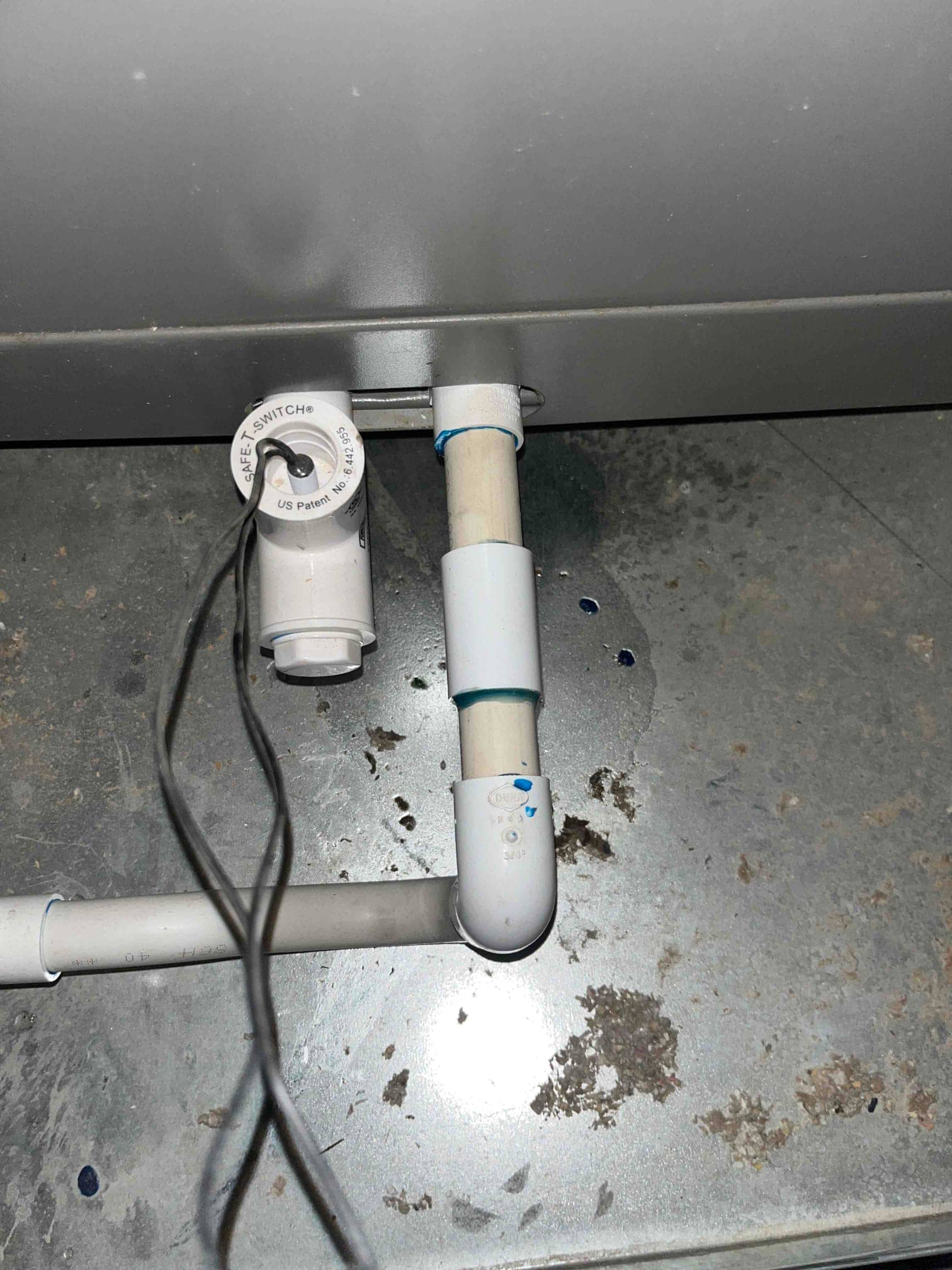 PVC condensate drain line with union and elbow under an air handler, showing wet area from recent leak or repair.