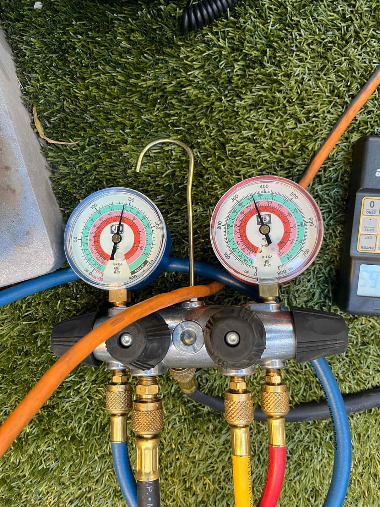Refrigerant manifold gauges connected to an HVAC system during service, showing analog low-side and high-side pressure dials without legible numeric readings.