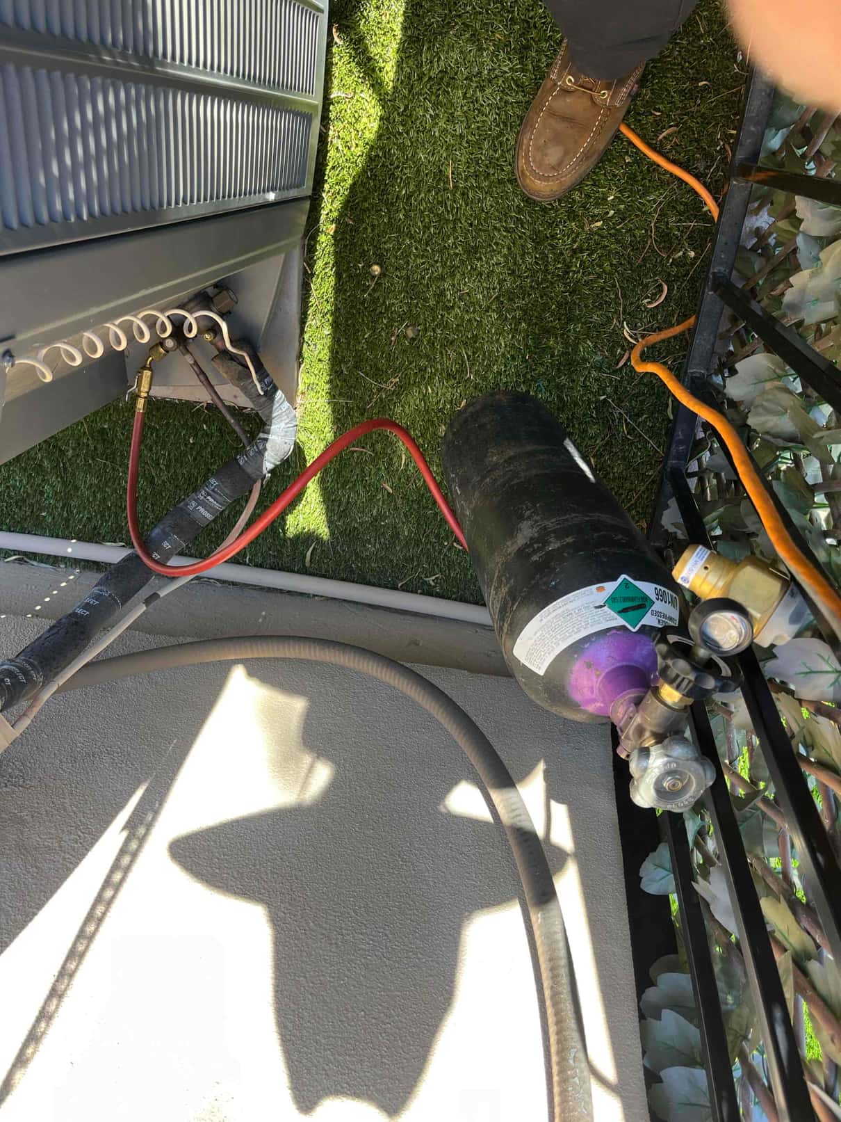 Refrigerant recovery cylinder connected to the outdoor condenser service port with red hose during compressor replacement work.