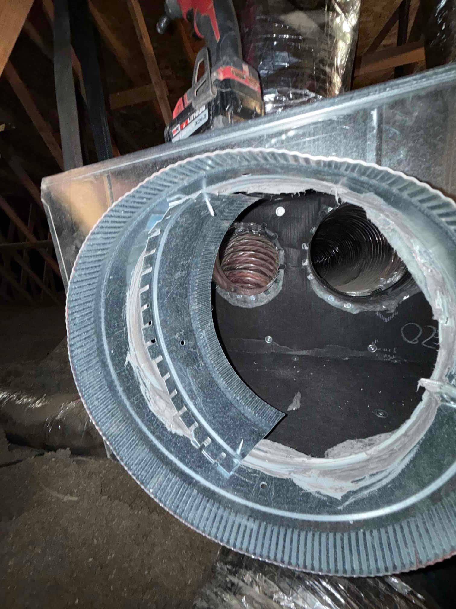 Round duct takeoff with mastic sealant installed on a metal plenum in the attic, flexible ducts visible in background.