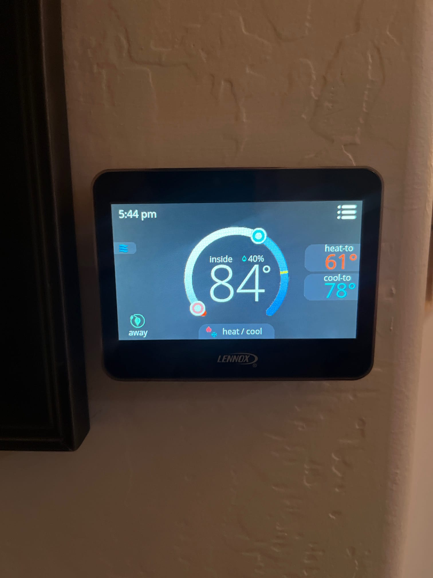 Smart thermostat display shows inside temperature at 84°F with system set to heat/cool mode on a wall.