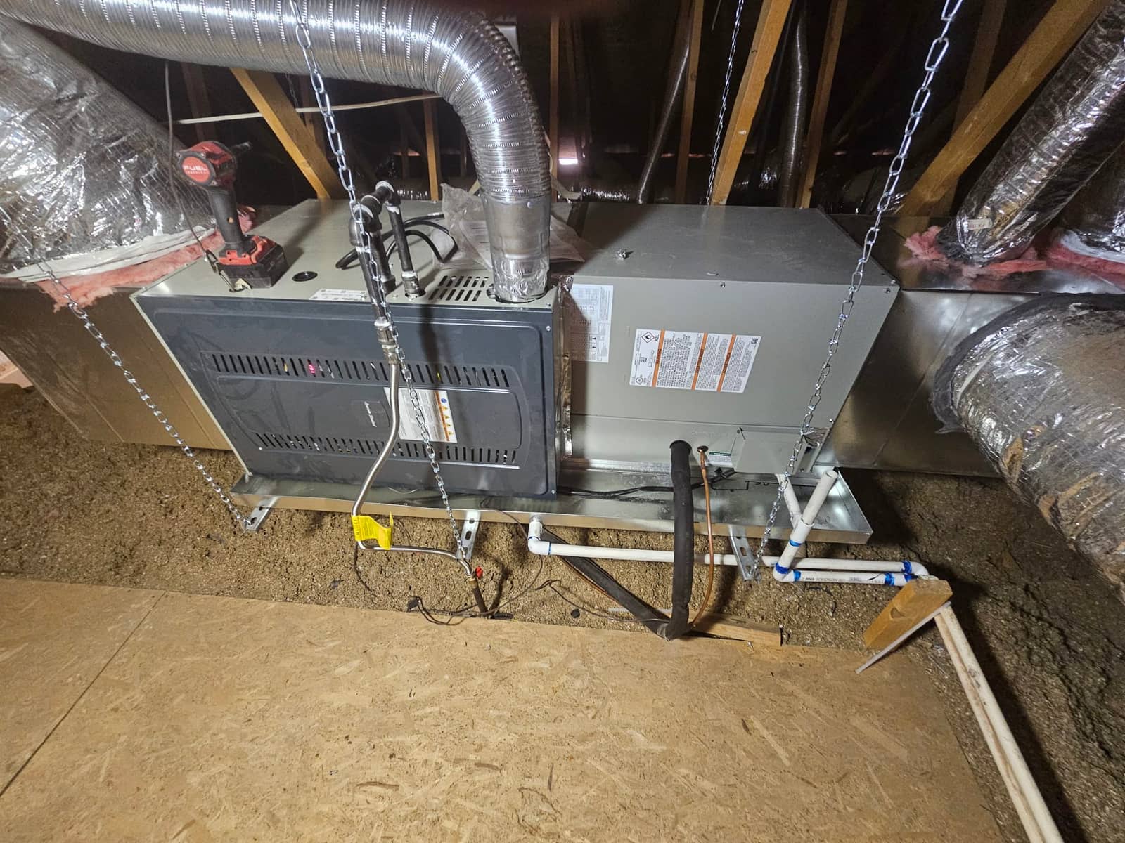 Suspended air handler and furnace assembly installed in attic with insulated duct connections and PVC condensate drain piping routed to a trap.
