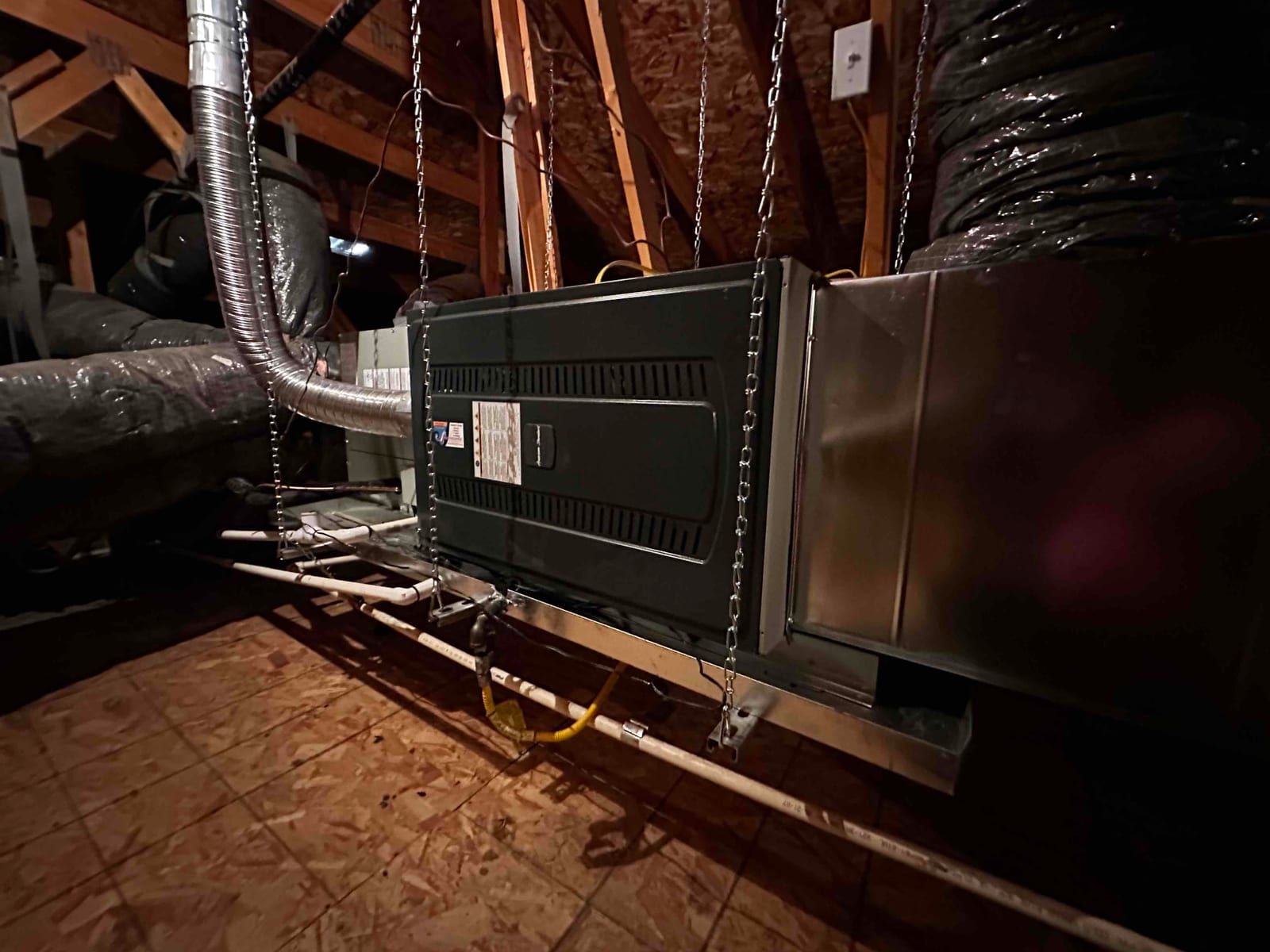 Suspended attic air handler with insulated duct connections, drain lines, and metal plenum installed on a hanging platform.