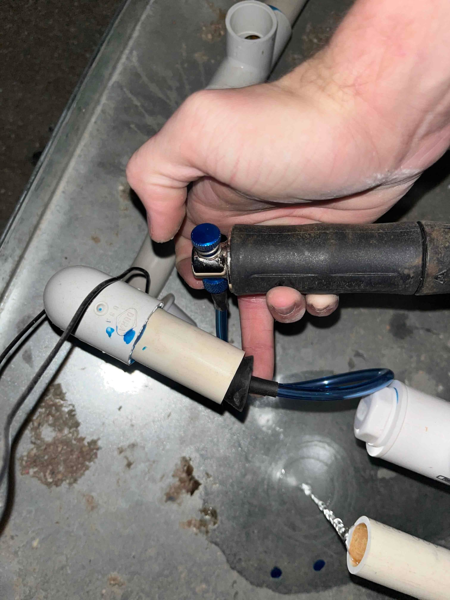 Technician secures a blue condensate drain line with a hose clamp during PVC drain repair inside the air handler.