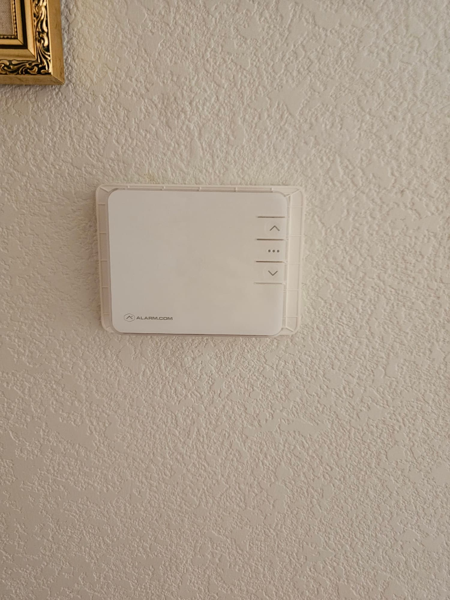 Wall-mounted low-profile thermostat installed and leveled on textured interior wall, with simple up and down control buttons.