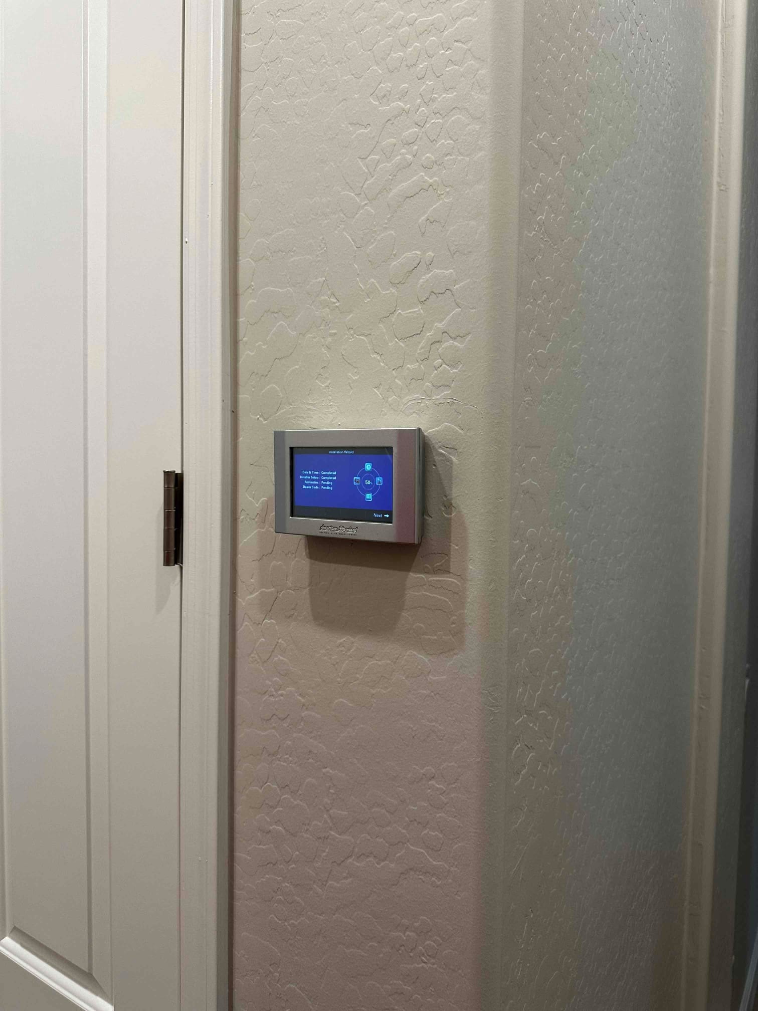 Wall-mounted smart thermostat installed and powered on in the hallway, displaying the home screen interface.