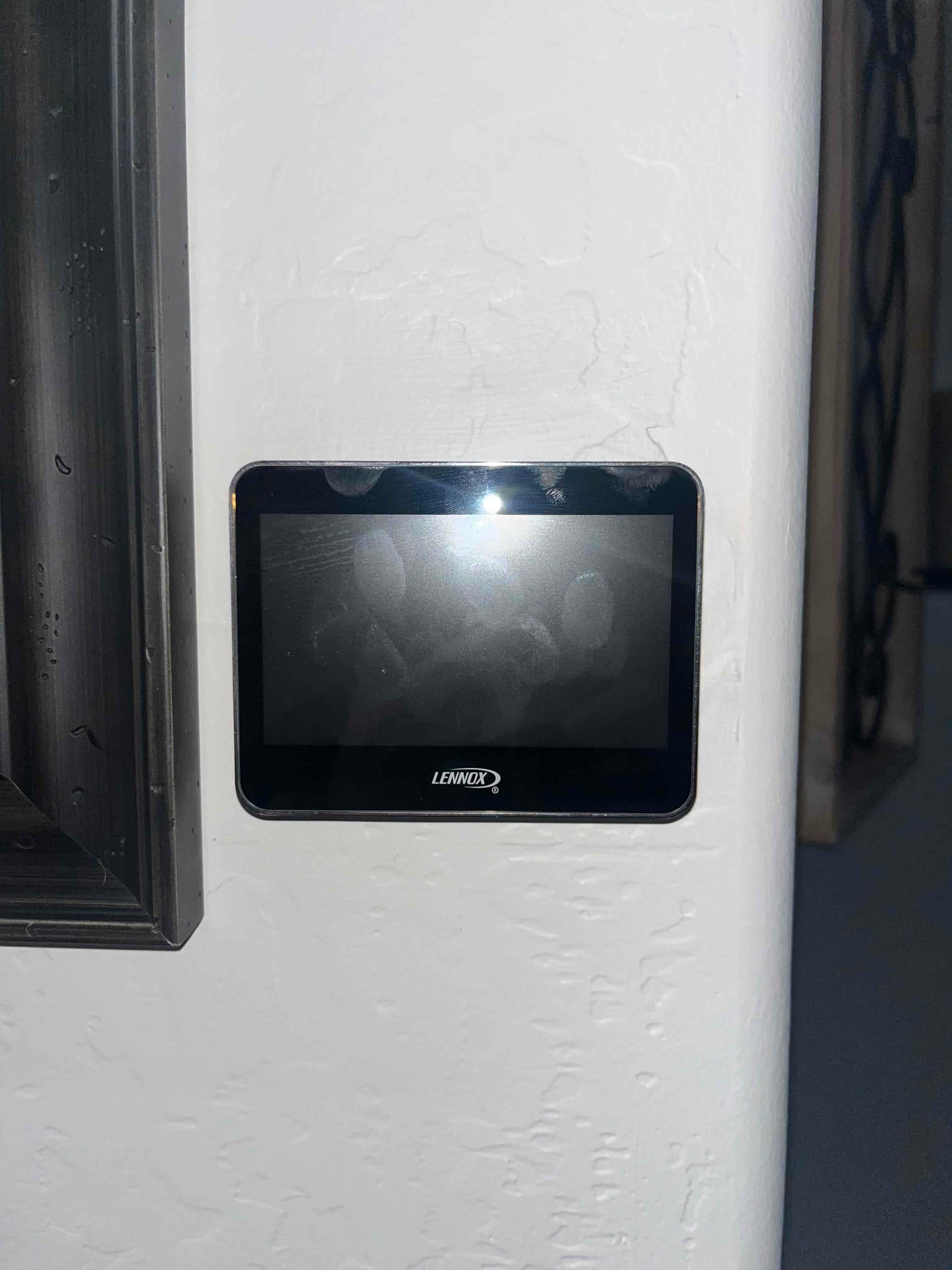 Wall-mounted touchscreen thermostat with a dark display and visible smudges on the screen surface.