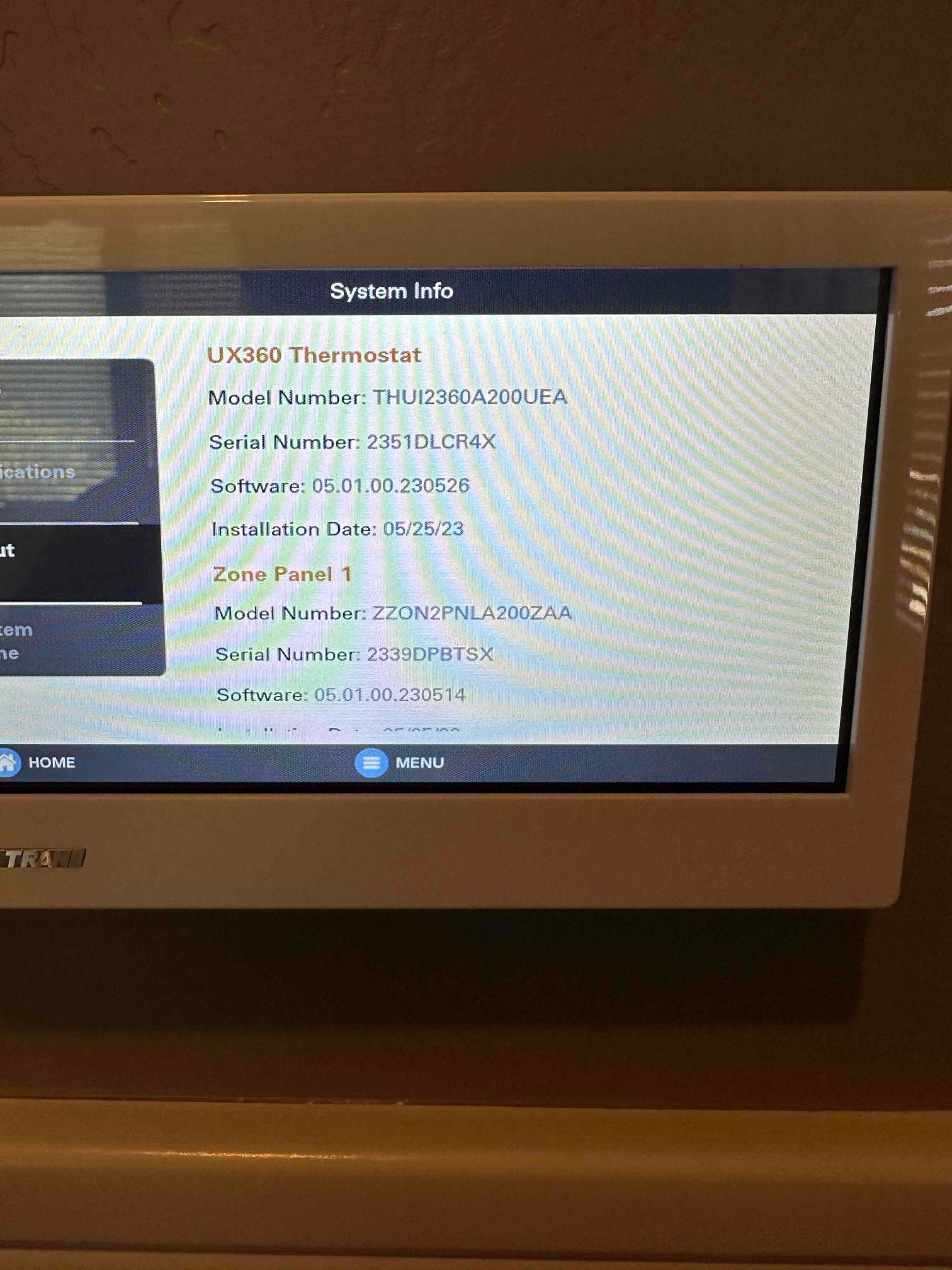 Wall-mounted touchscreen thermostat displays system information and menu, showing installation details and software version on the screen.