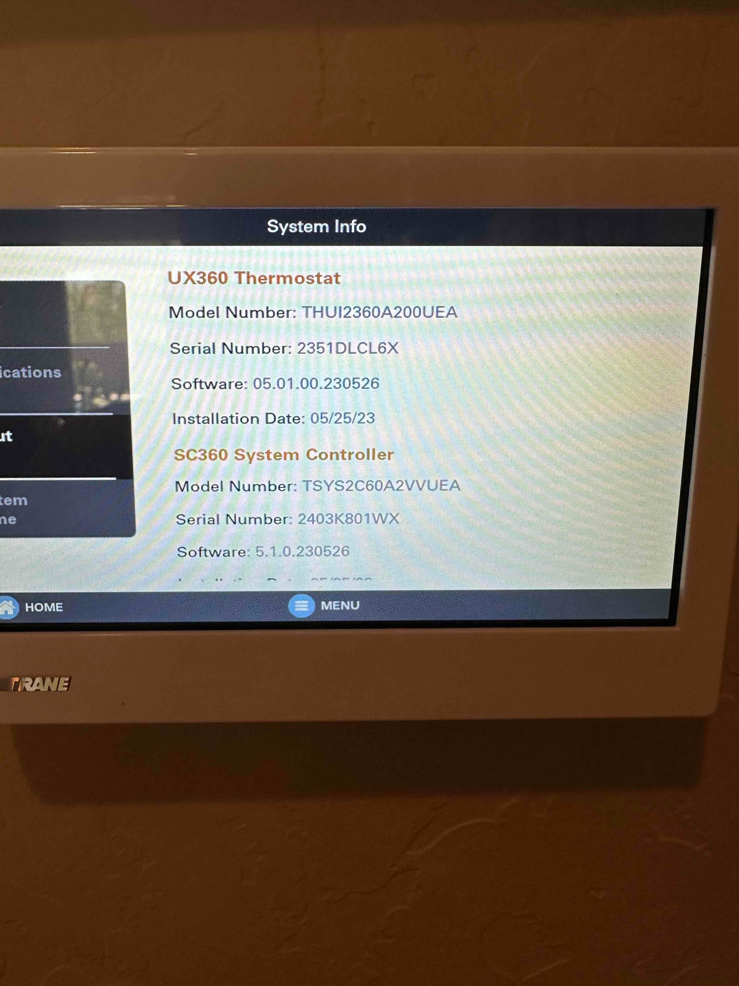 Wall-mounted touchscreen thermostat displays system information screen with thermostat and system controller details during setup.