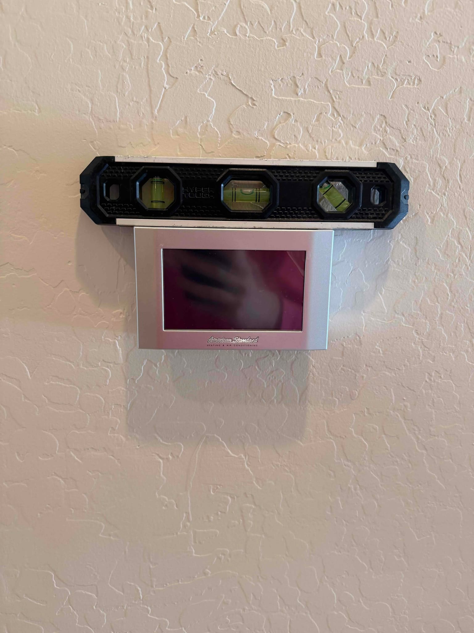 Wall-mounted touchscreen thermostat being leveled during installation, ensuring proper alignment on the finished interior wall.