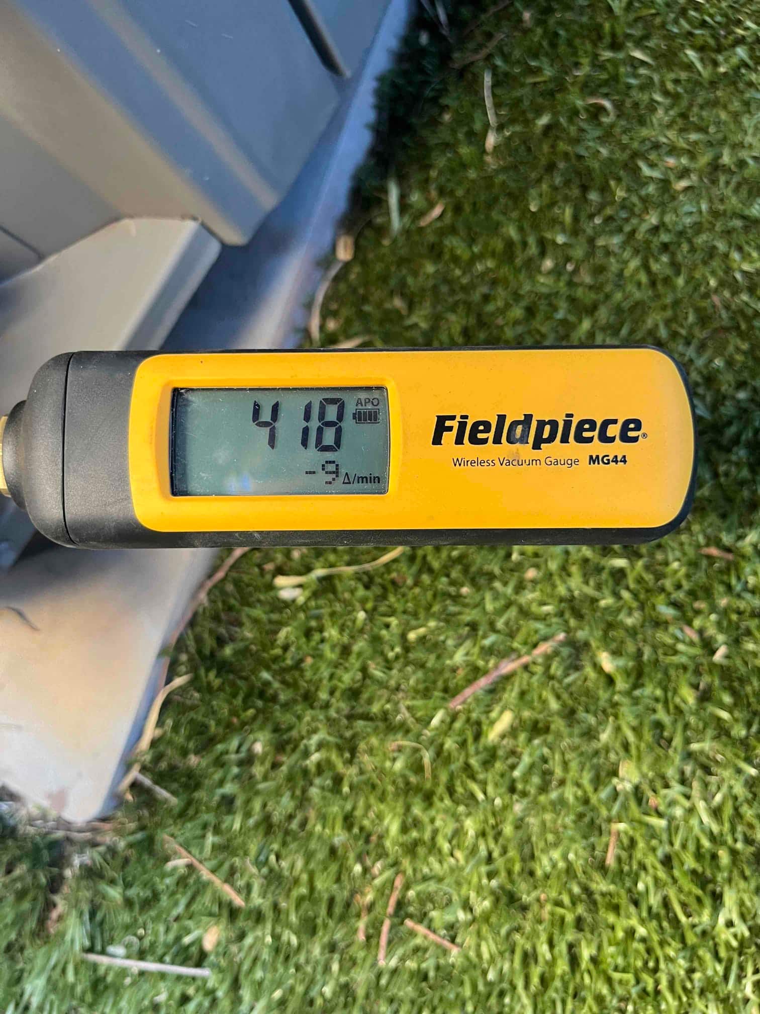 Wireless vacuum gauge shows 418 microns during system evacuation beside the outdoor condenser unit.