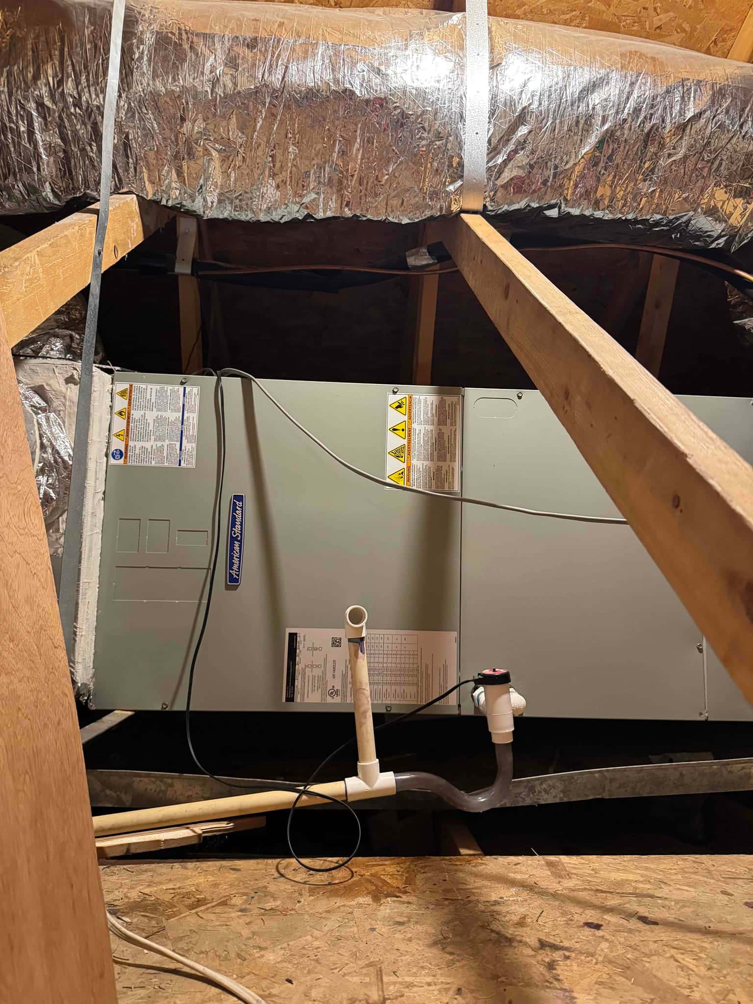 Air handler in attic with PVC condensate drain line, cleanout, and float safety switch visible along the drain.
