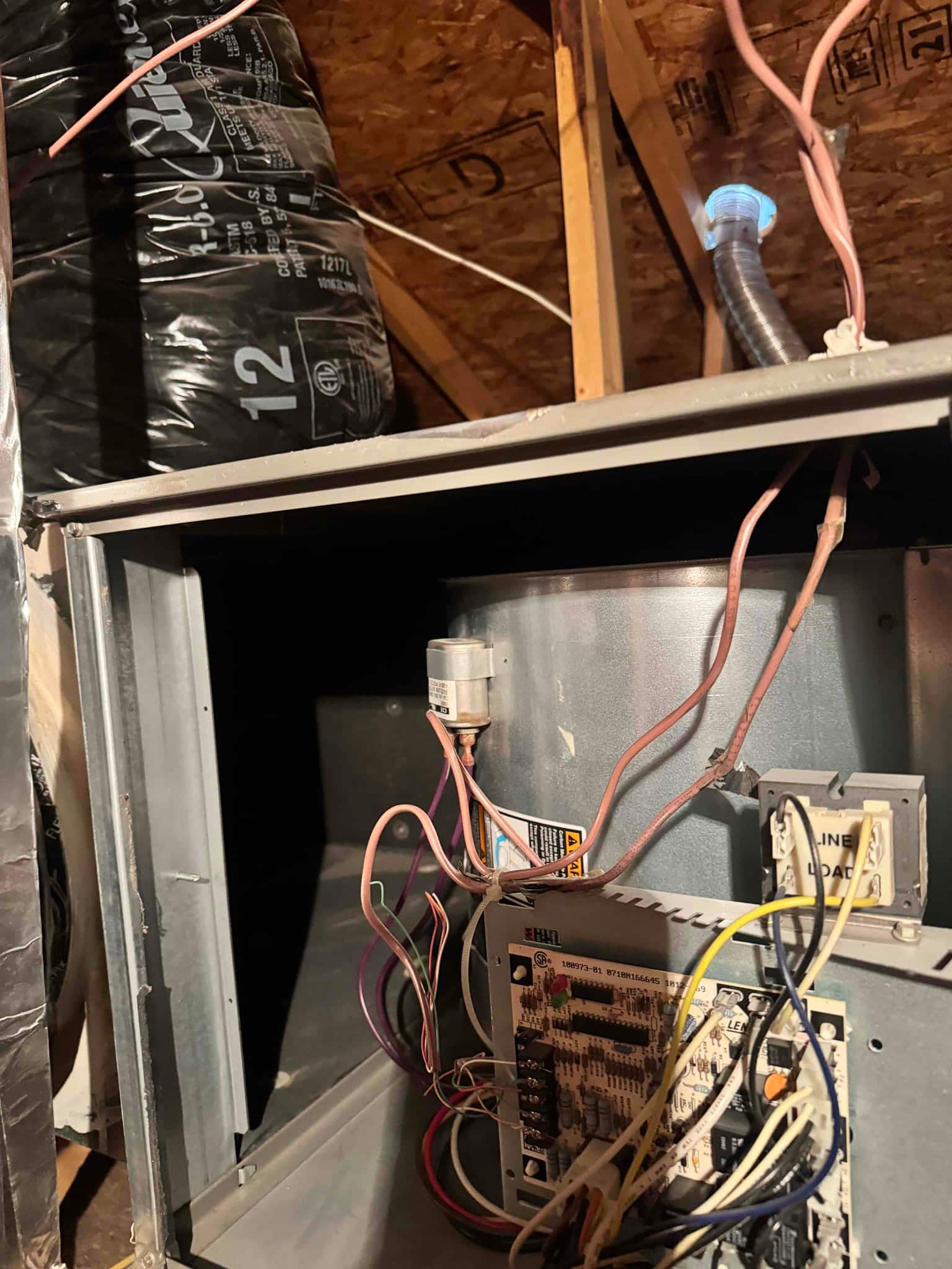 Air handler cabinet open in attic, showing blower housing, control board with wiring, and installed ionizing air scrubber module.