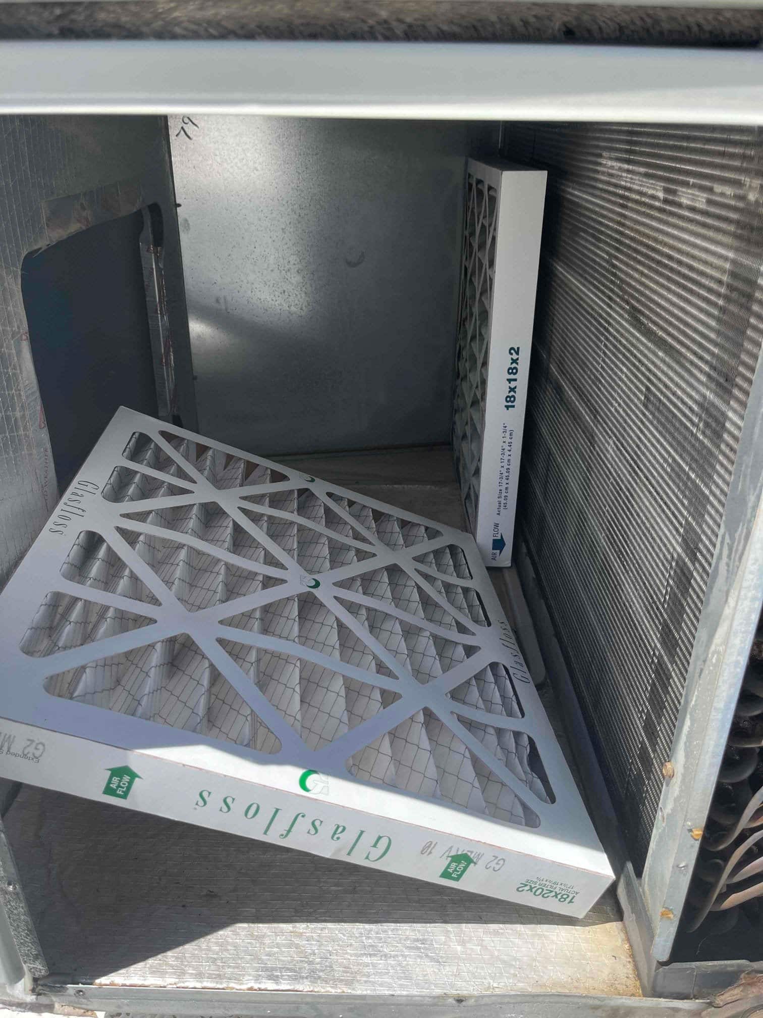 Air handler cabinet open with two pleated air filters, showing coil surface and filter size markings visible on packaging.
