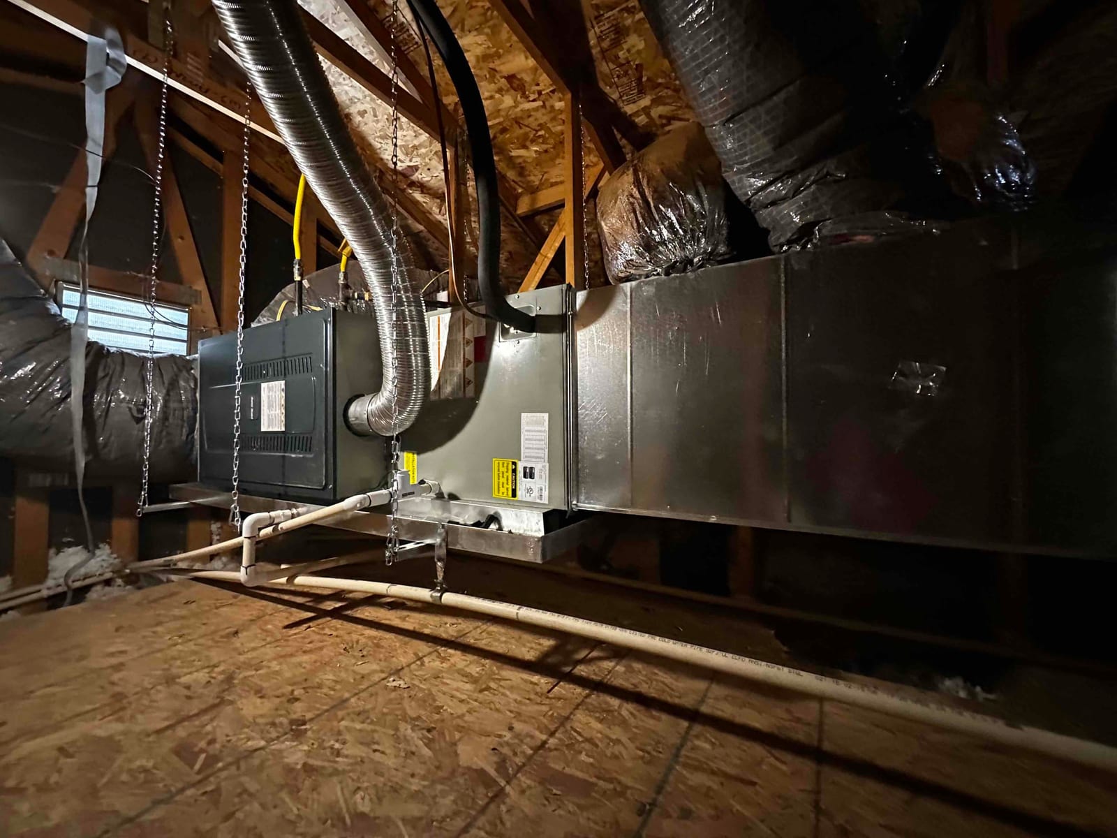 Air handler and ductwork suspended in attic with condensate drain, flexible connections, and sheet metal plenum installed on support chains.