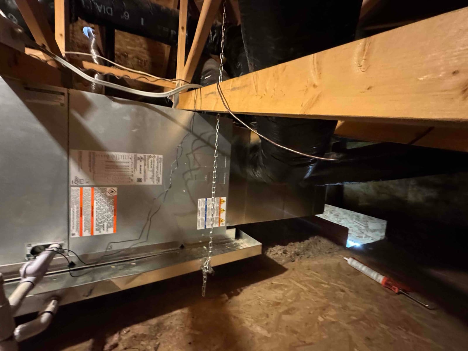 Air handler installed on a suspended platform in the attic with connected PVC condensate drain and insulated ductwork.