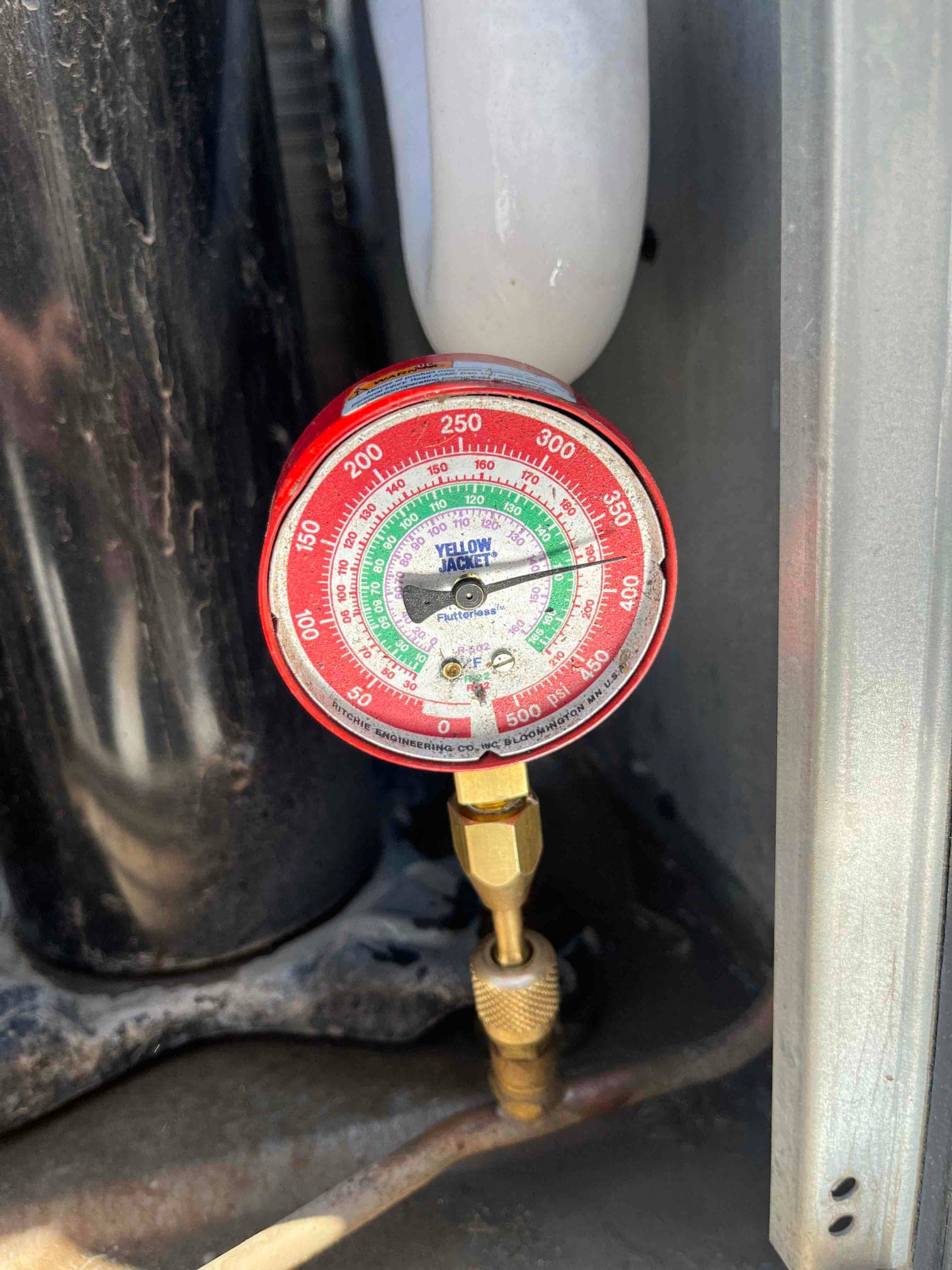 Analog manifold gauge connected on the low side shows approximately 105 psi during air conditioning system testing.