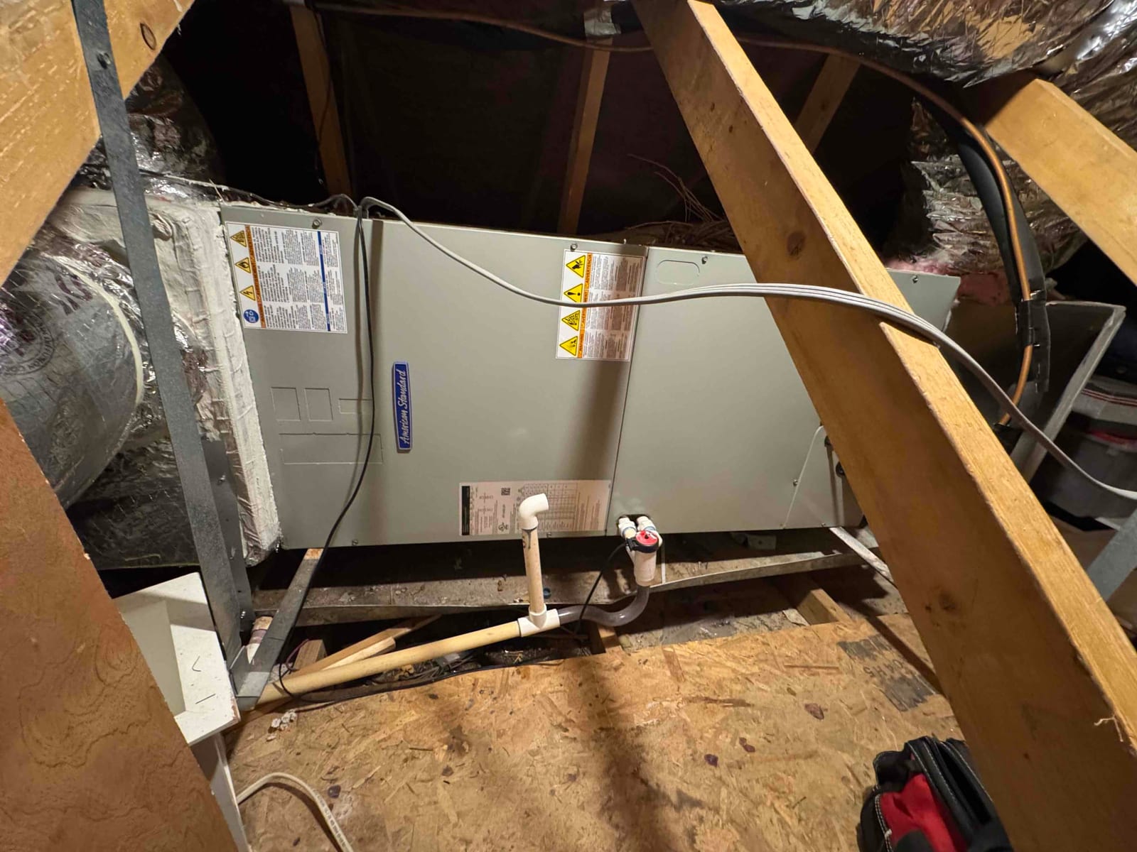 Attic air handler with PVC condensate drain piping and cleanout tee visible near the service panel.