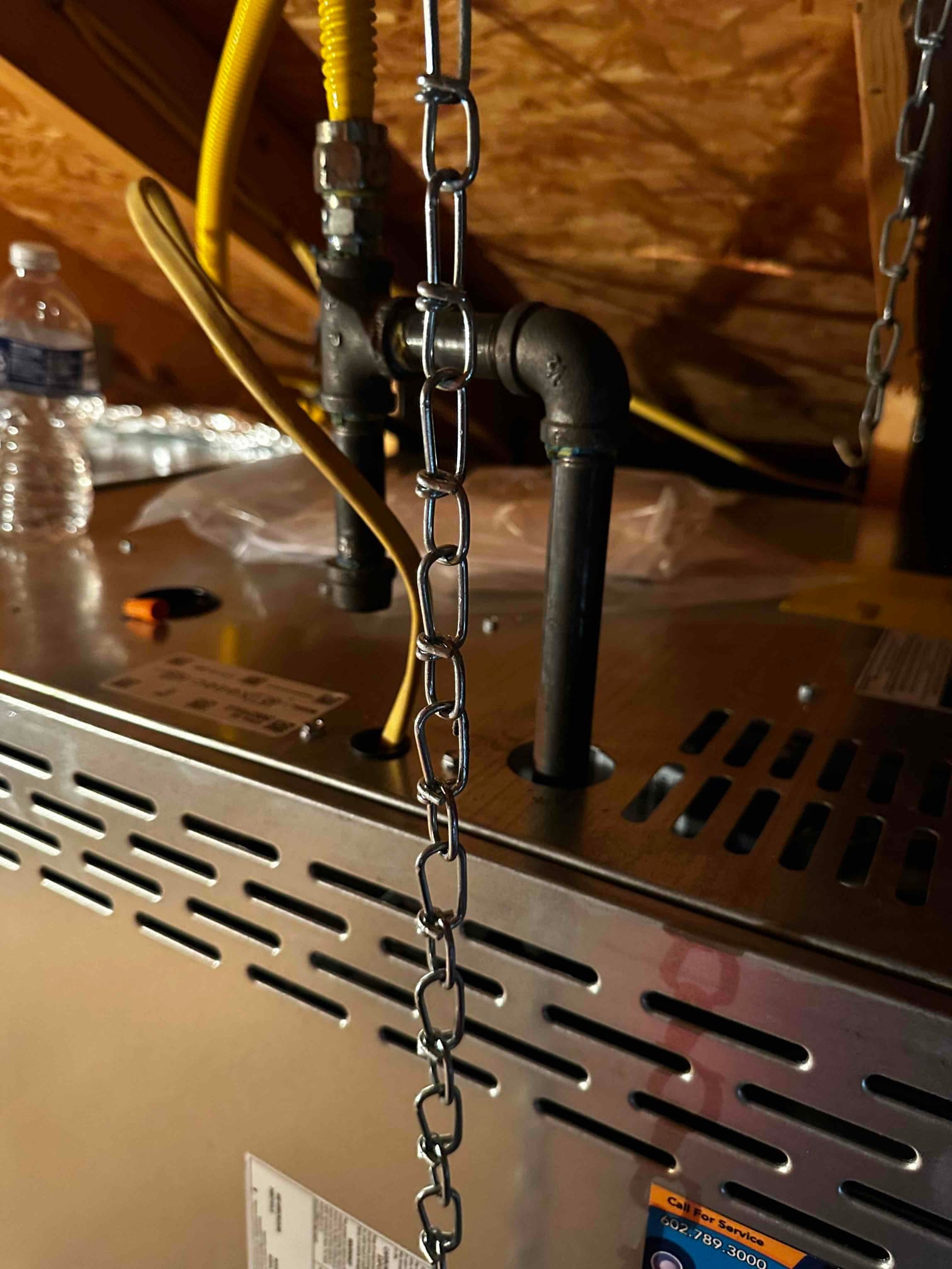 Attic furnace with connected black iron gas piping and yellow flexible gas connector, showing vented cabinet top and nearby support chains.