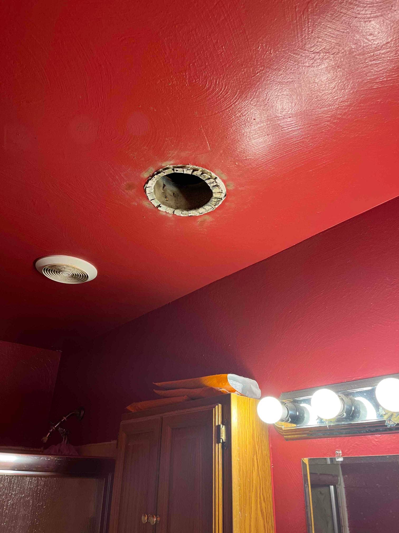 Ceiling cutout for a new supply duct in a bathroom, with existing ceiling vent and nearby vanity lights visible.