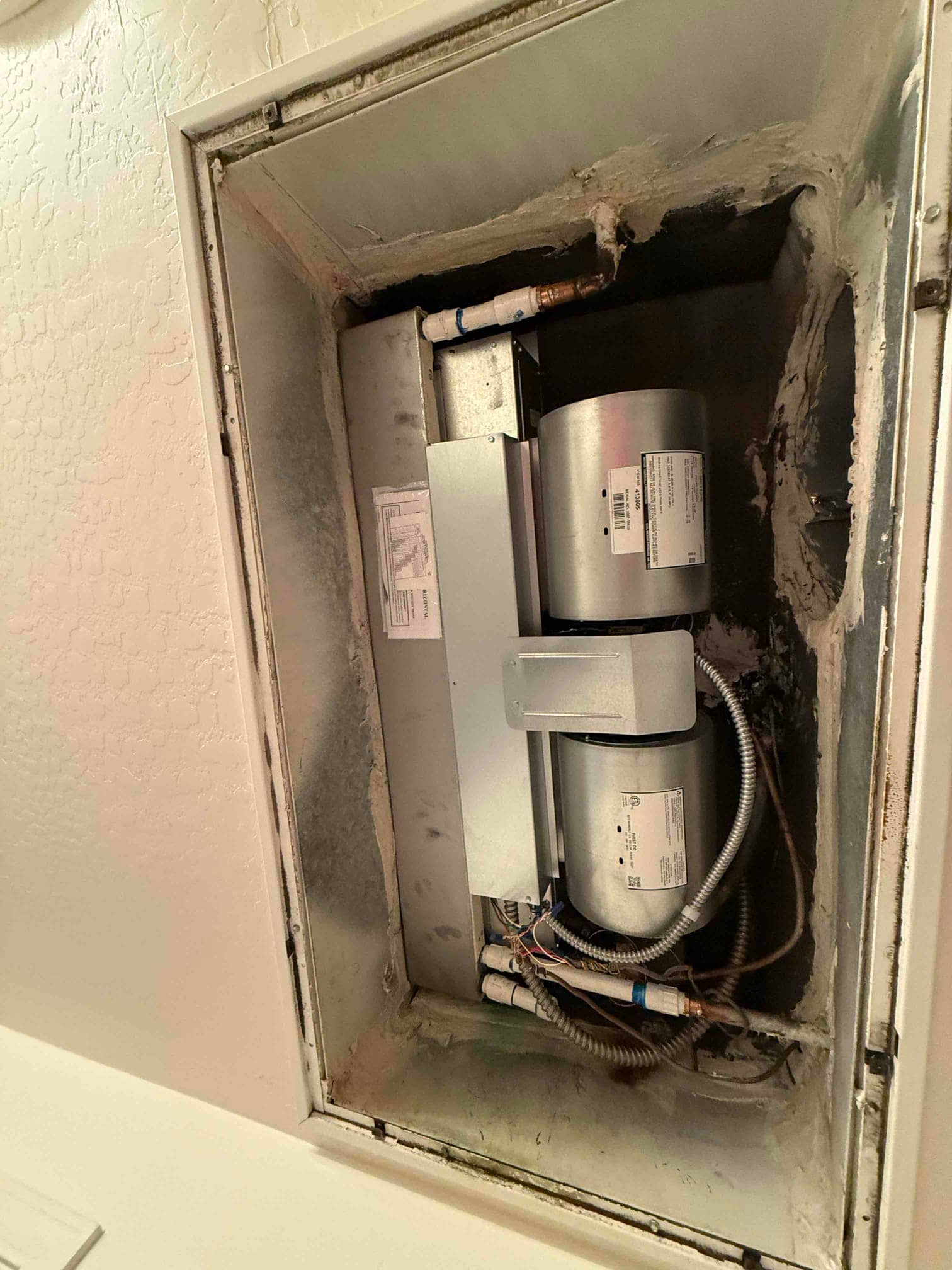 Ceiling-mounted air handler compartment open, showing blower assembly, electrical flex conduits, condensate piping, and sealed duct transitions.
