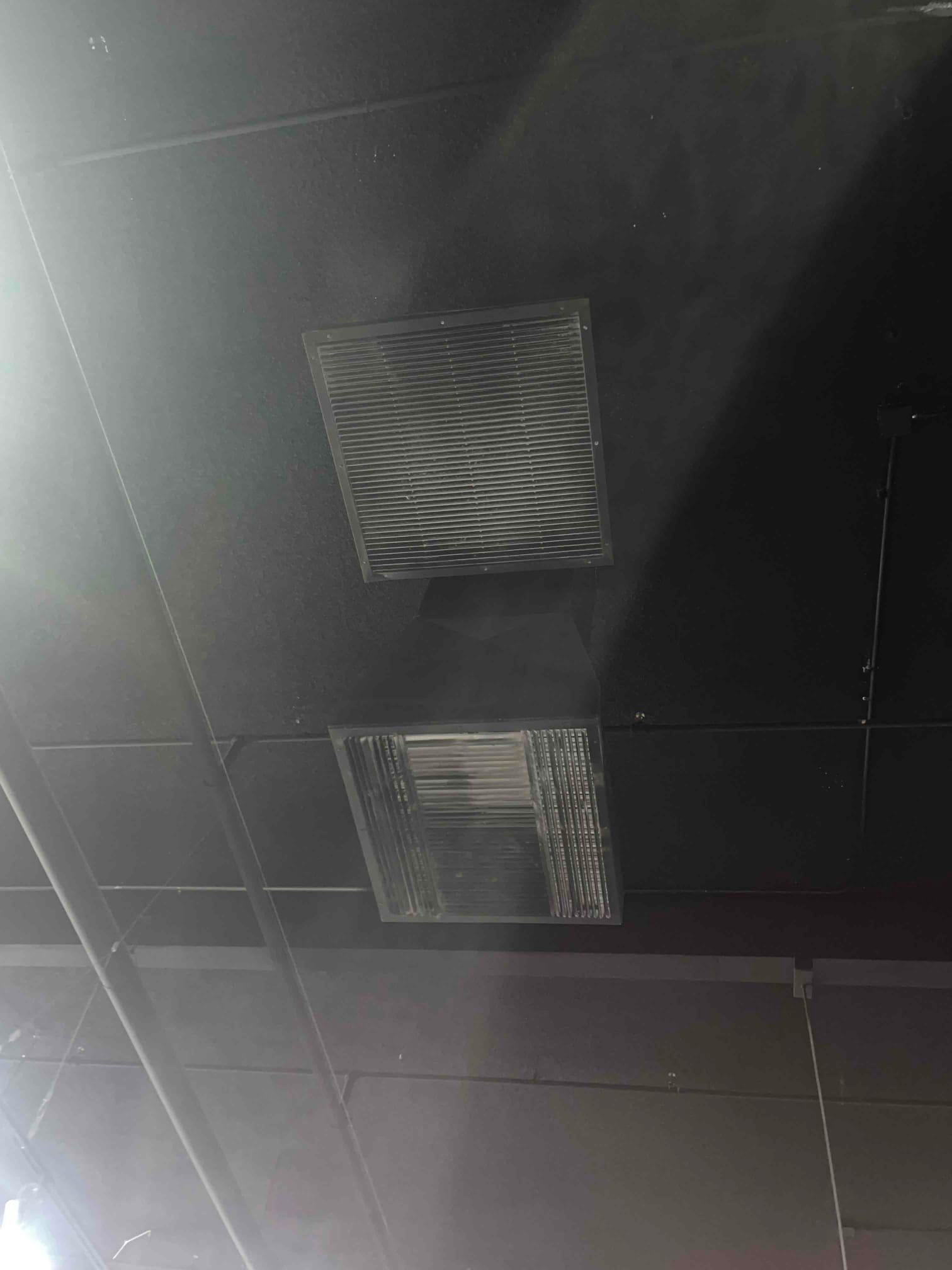 Ceiling-mounted return grille and supply diffuser visible on a dark suspended ceiling in a commercial space.