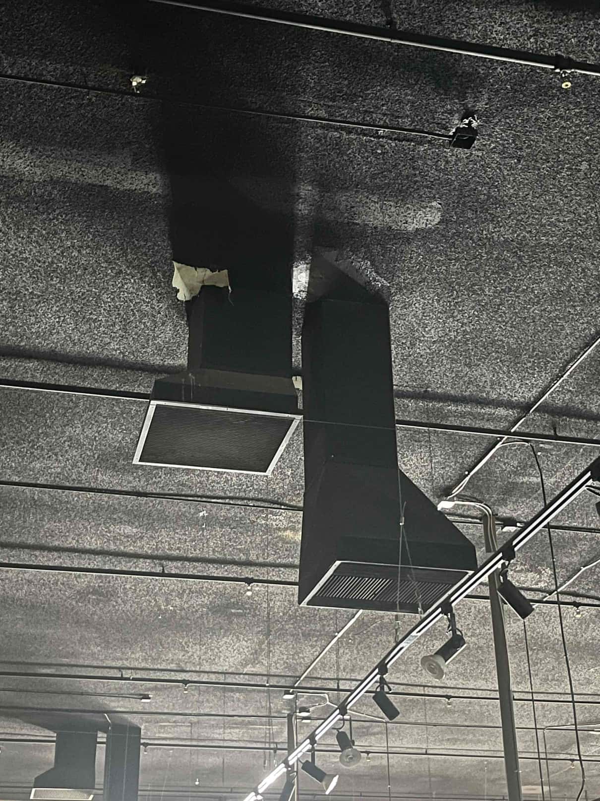 Ceiling-mounted return and supply air grilles with connected ductwork shown above track lighting in a commercial space.