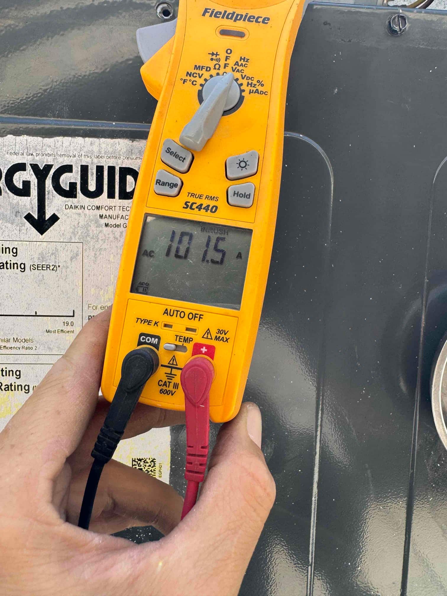 Clamp meter displays 10.15 A AC current with probes connected to the HVAC equipment wiring inside the unit.