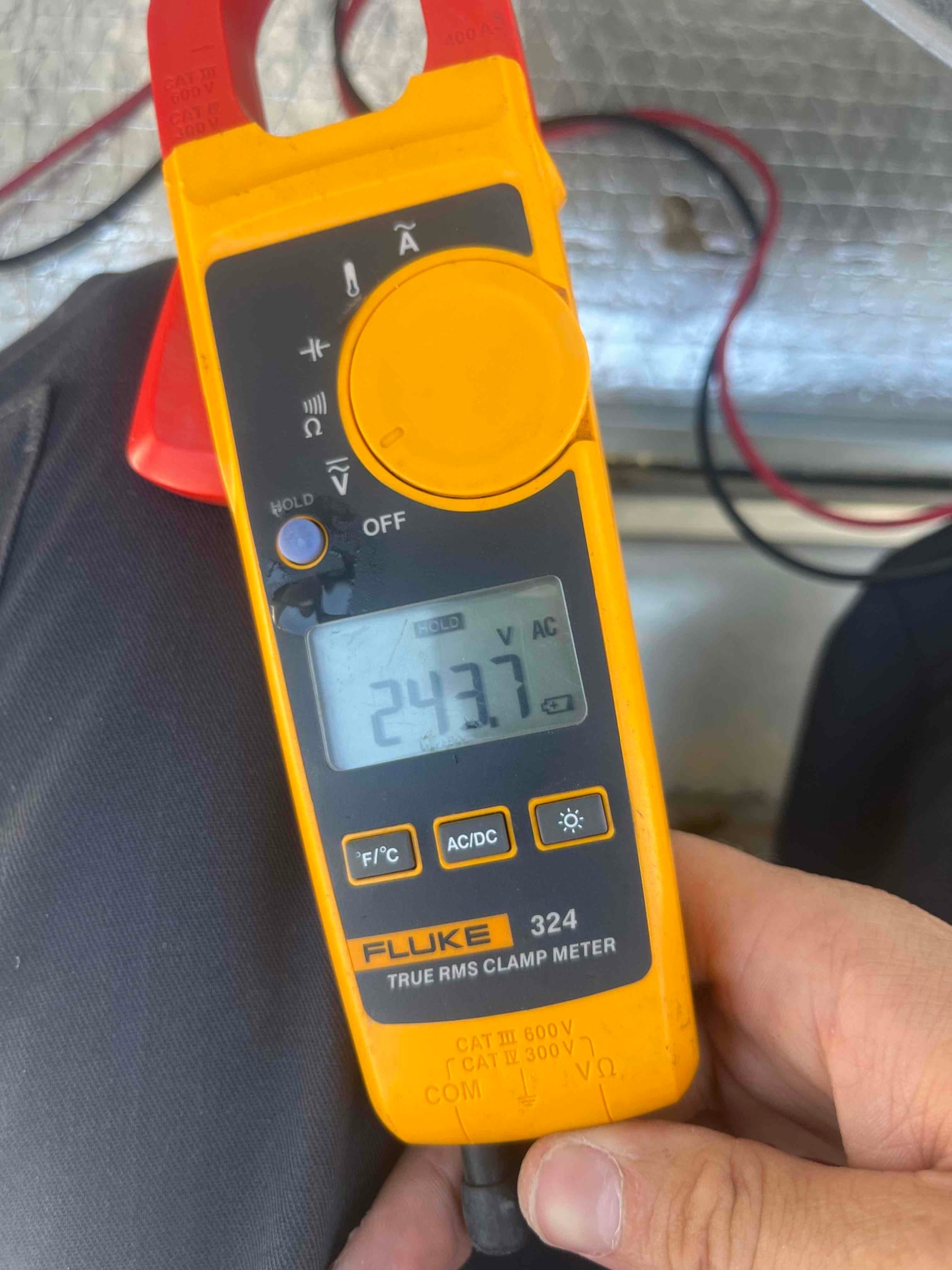 Clamp meter displays 243.7 V AC while measuring voltage with test leads connected to the system wiring.