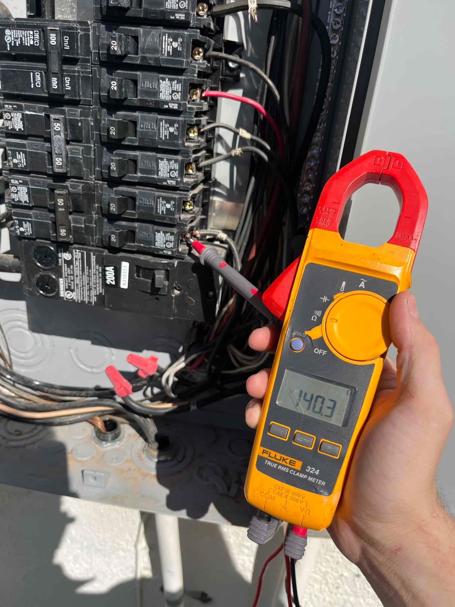 Clamp meter measures 140.3 V at a breaker connection using the test probes inside an electrical panel.