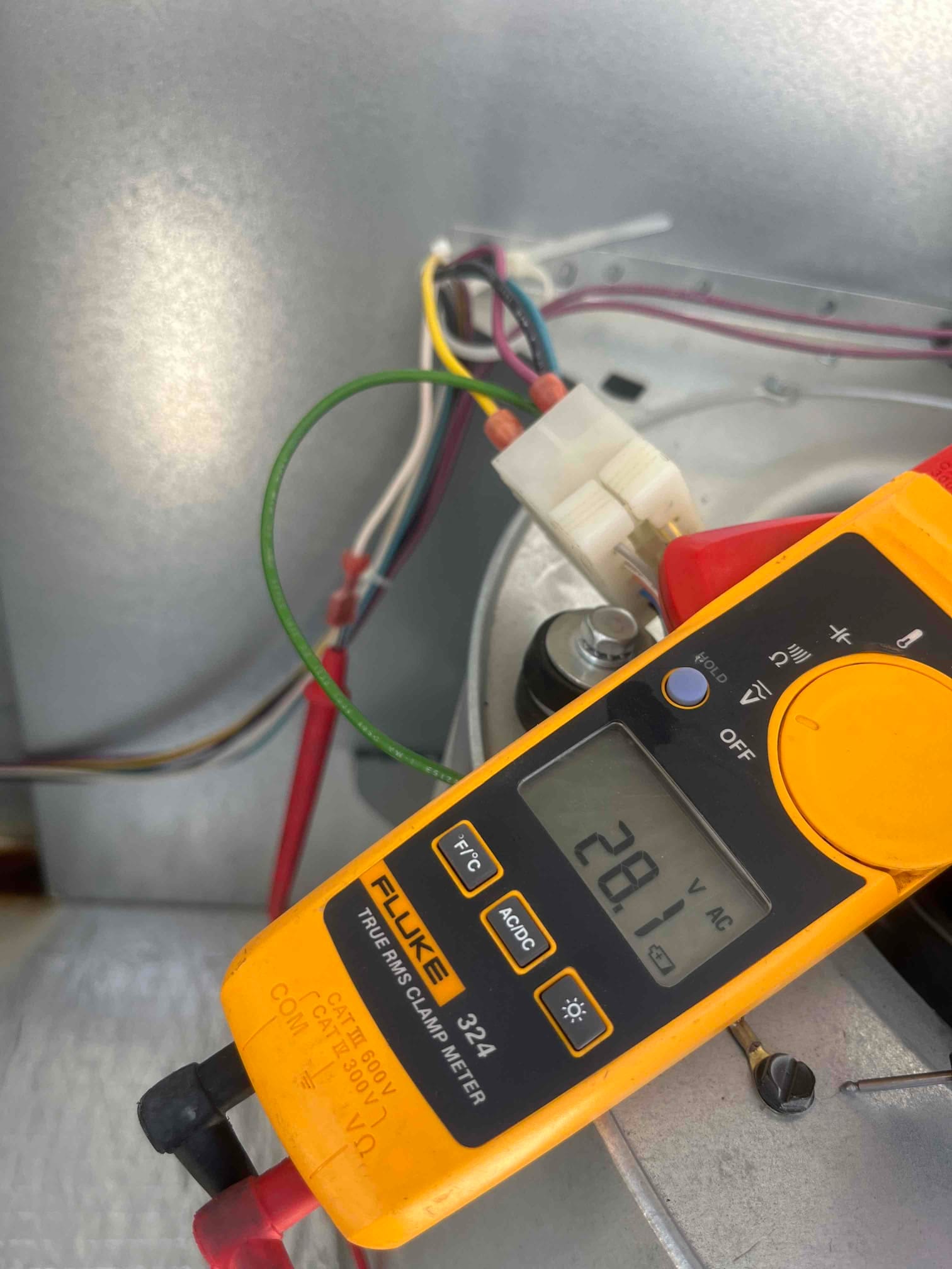 Clamp meter measures 28.1 V AC on indoor blower wiring inside the air handler compartment.