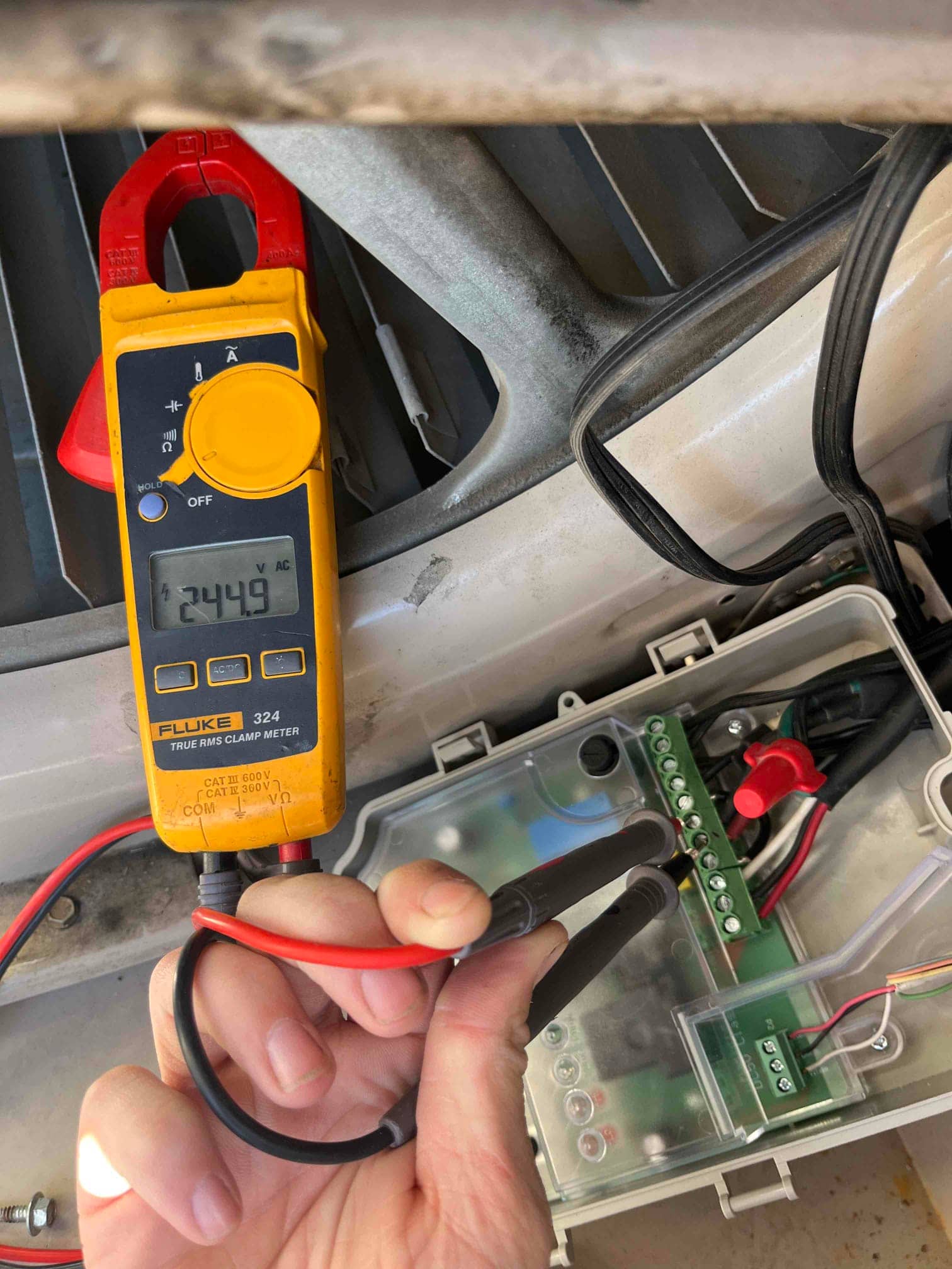 Clamp meter shows 244.9 V across terminals at the control wiring block inside the outdoor unit’s junction box.